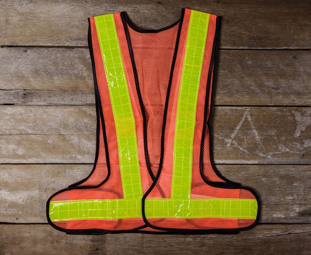 Chaleco de seguridad reflectante de color naranja y amarillo neón sobre fondo de madera.