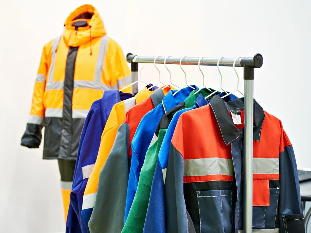 Ropa de trabajo en perchas; chaqueta de alta visibilidad en maniquí. Colores surtidos, bandas reflectantes.