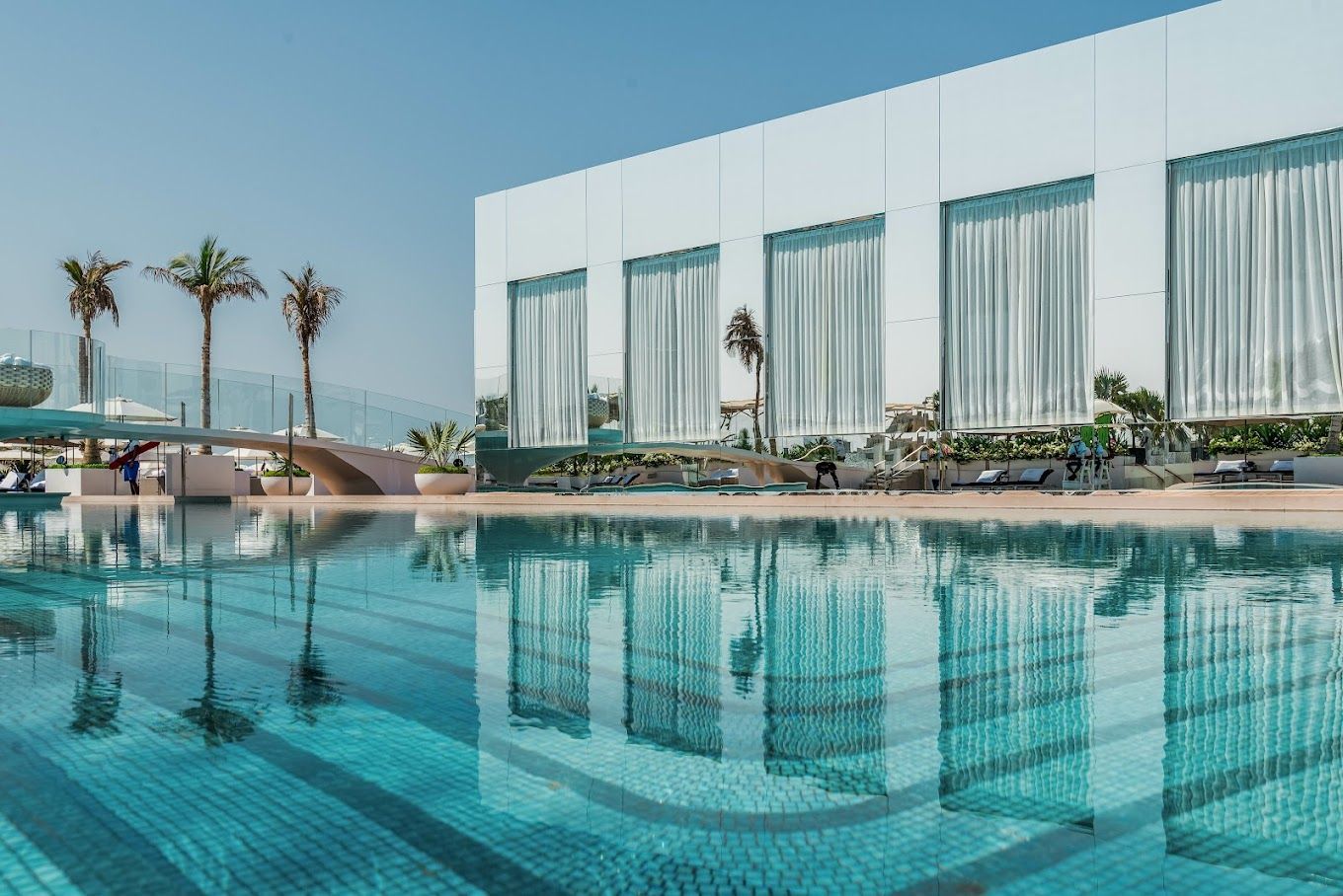 A large swimming pool in front of a building with palm trees in the background.