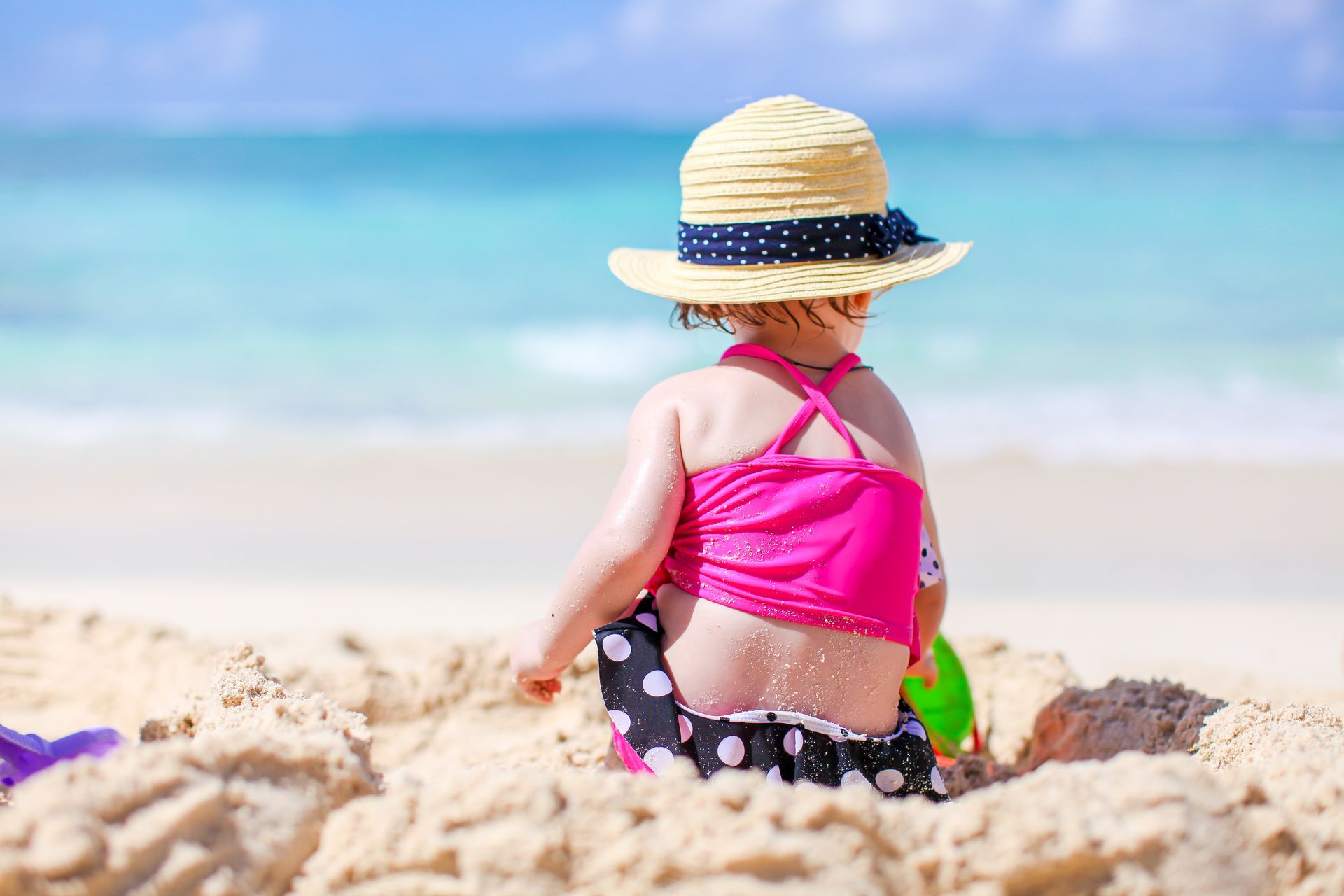 A little girl is sitting in the sand on the beach.