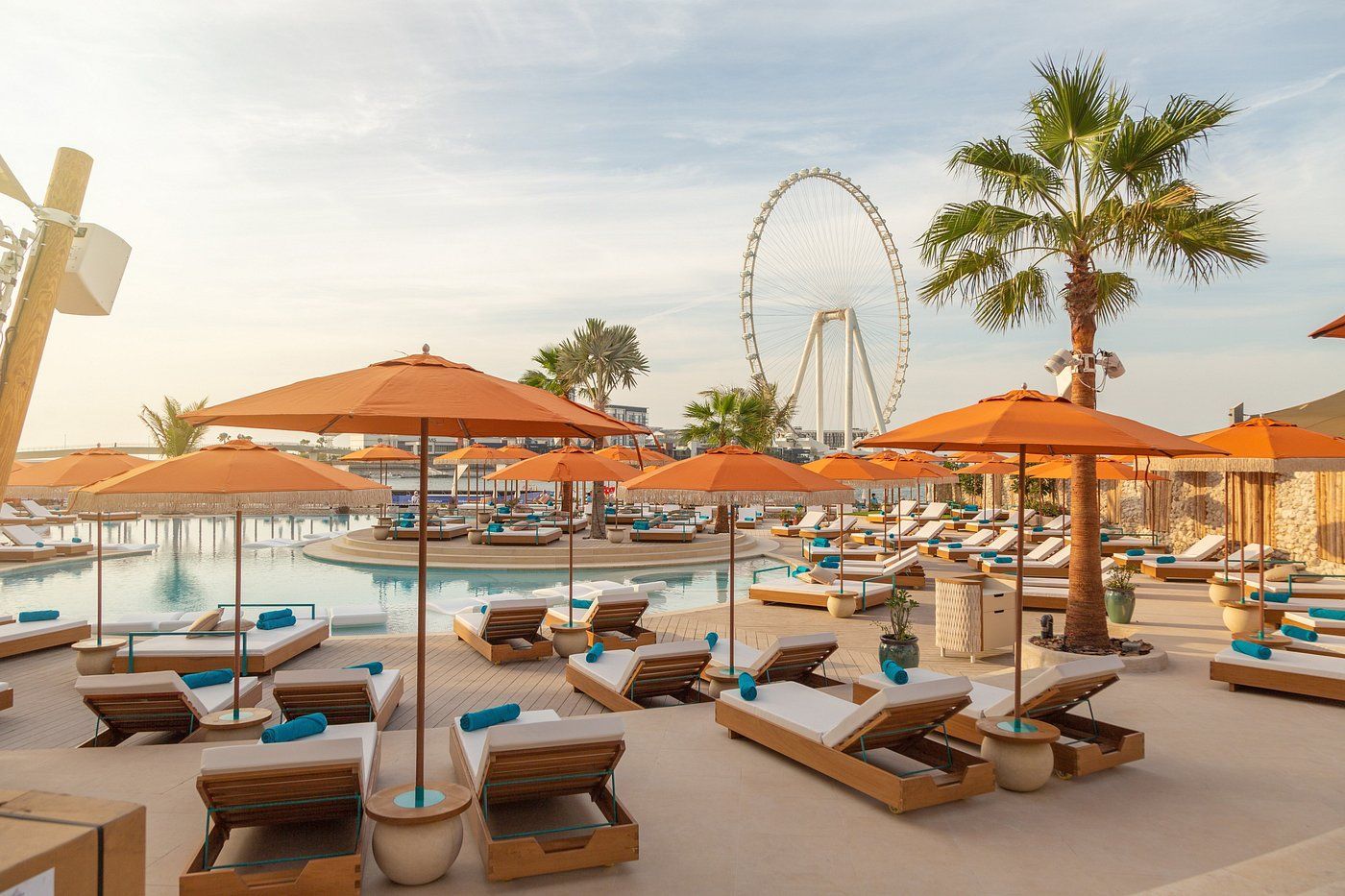 A ferris wheel is in the background of a swimming pool filled with umbrellas and chairs.