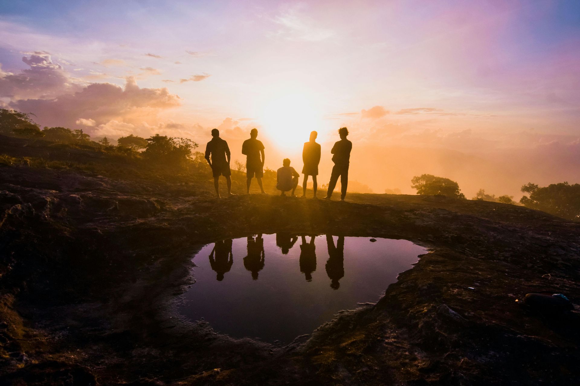 A group of people are standing next to a pond at sunset.