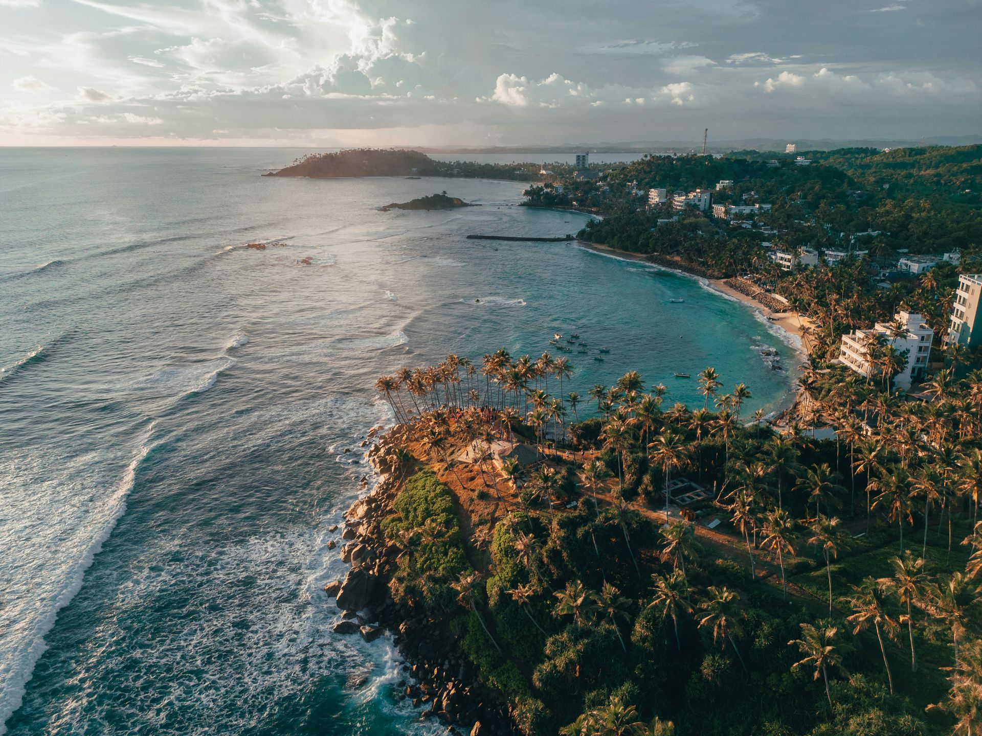 An aerial view of a beach with palm trees and a city in the distance.