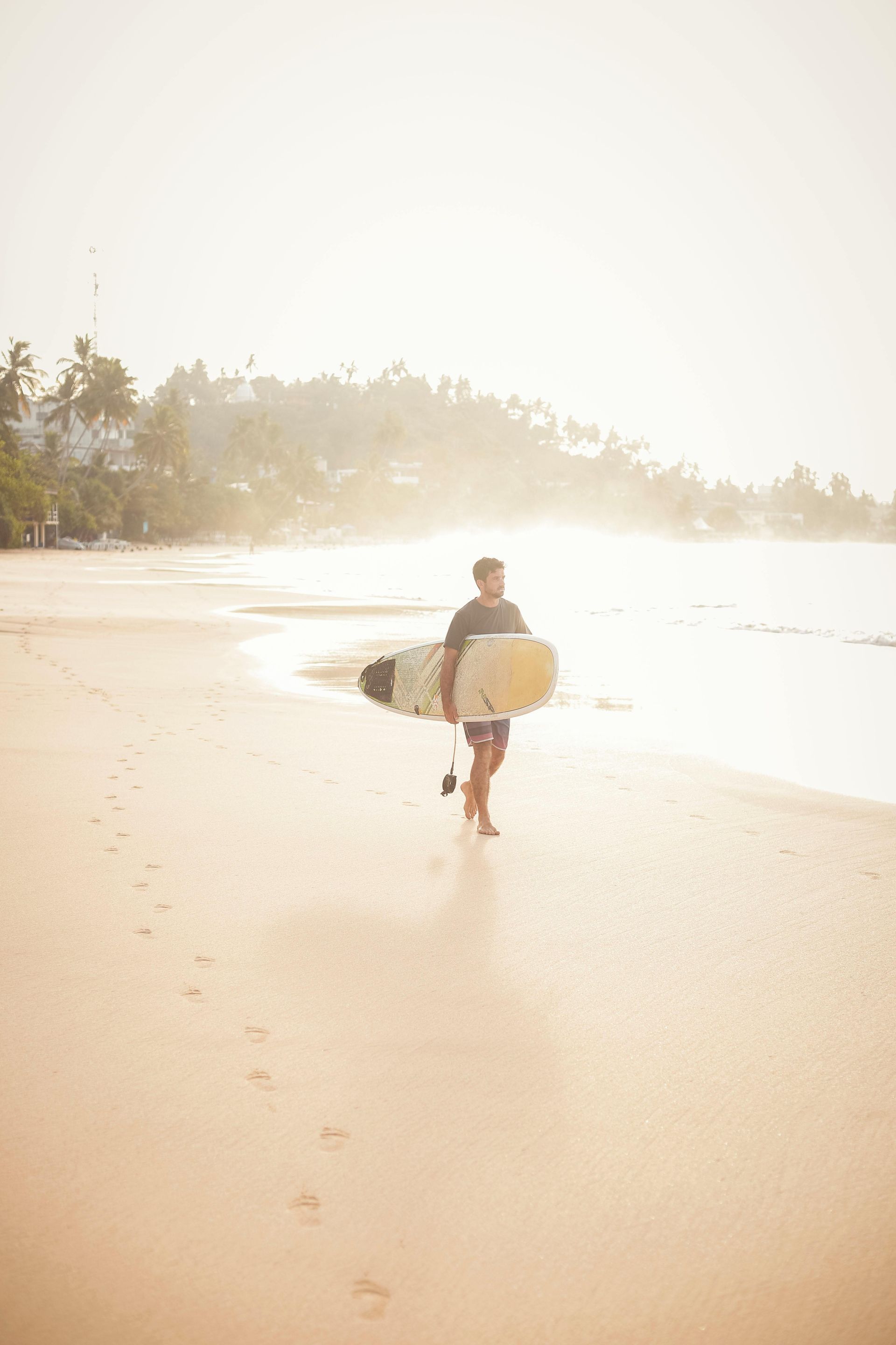A man is walking on the beach carrying a surfboard.