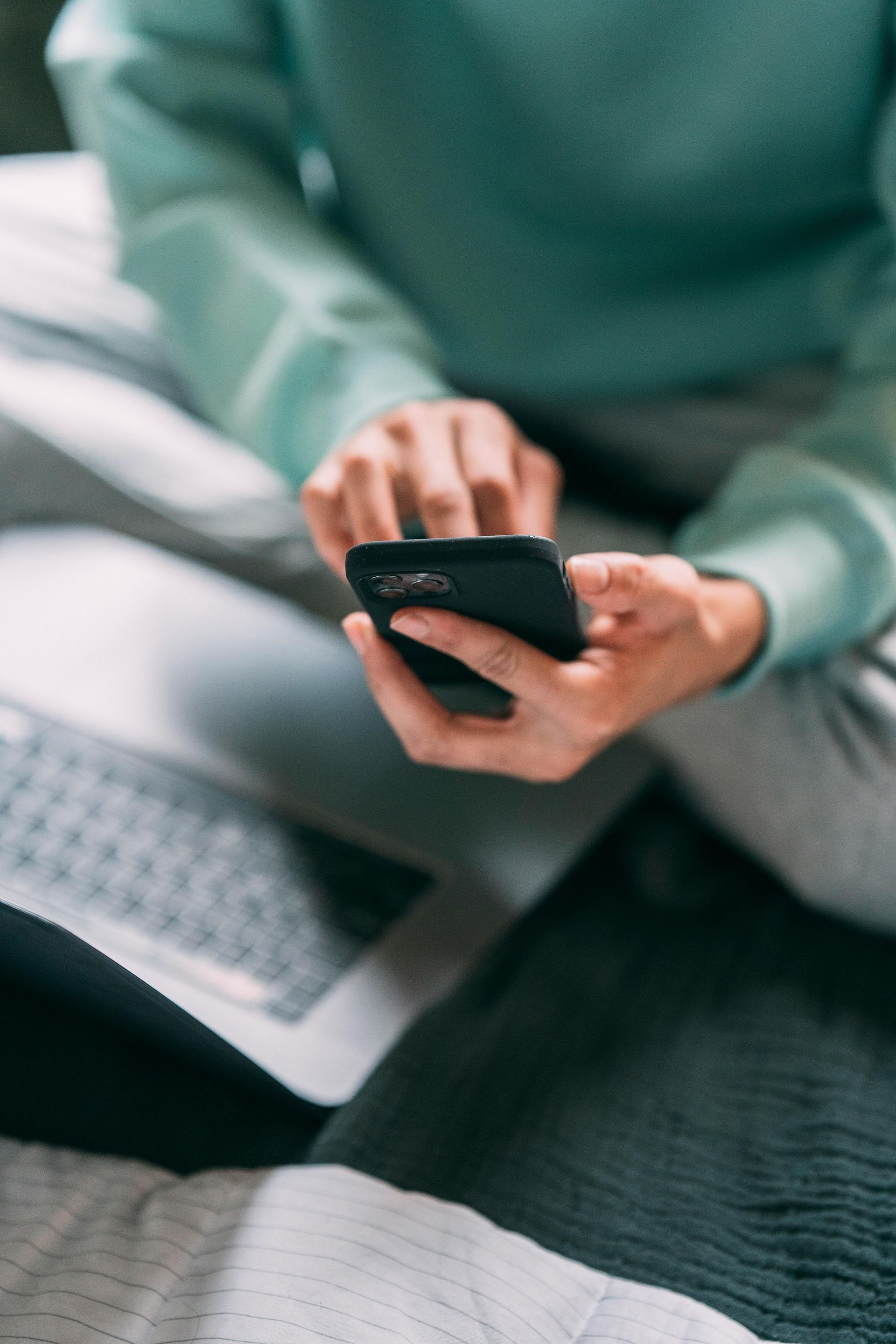 A woman is sitting on a bed using a cell phone.