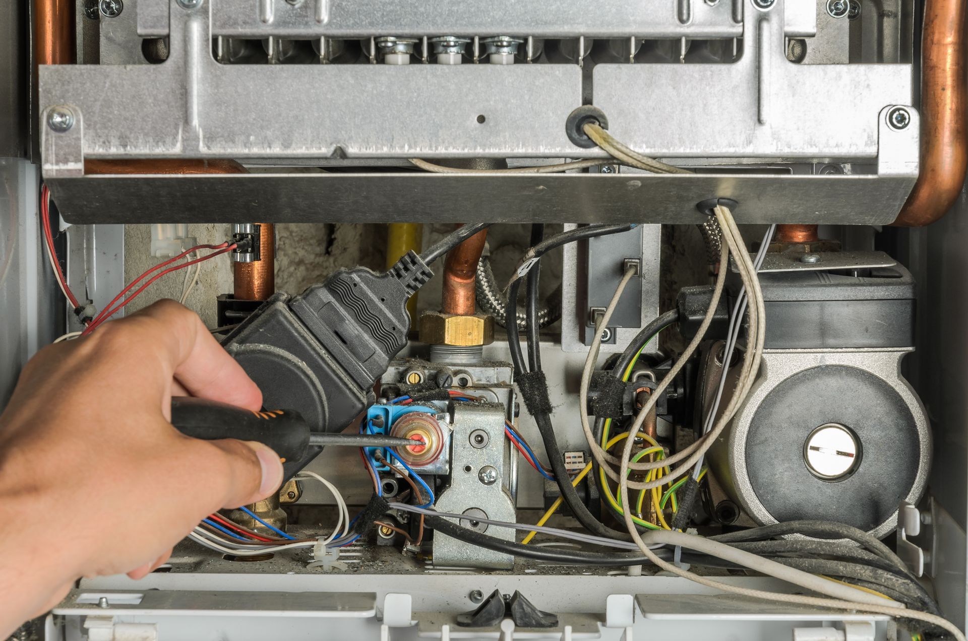 Hand checking wiring inside an open appliance, with circuit board, wires, and fan visible.