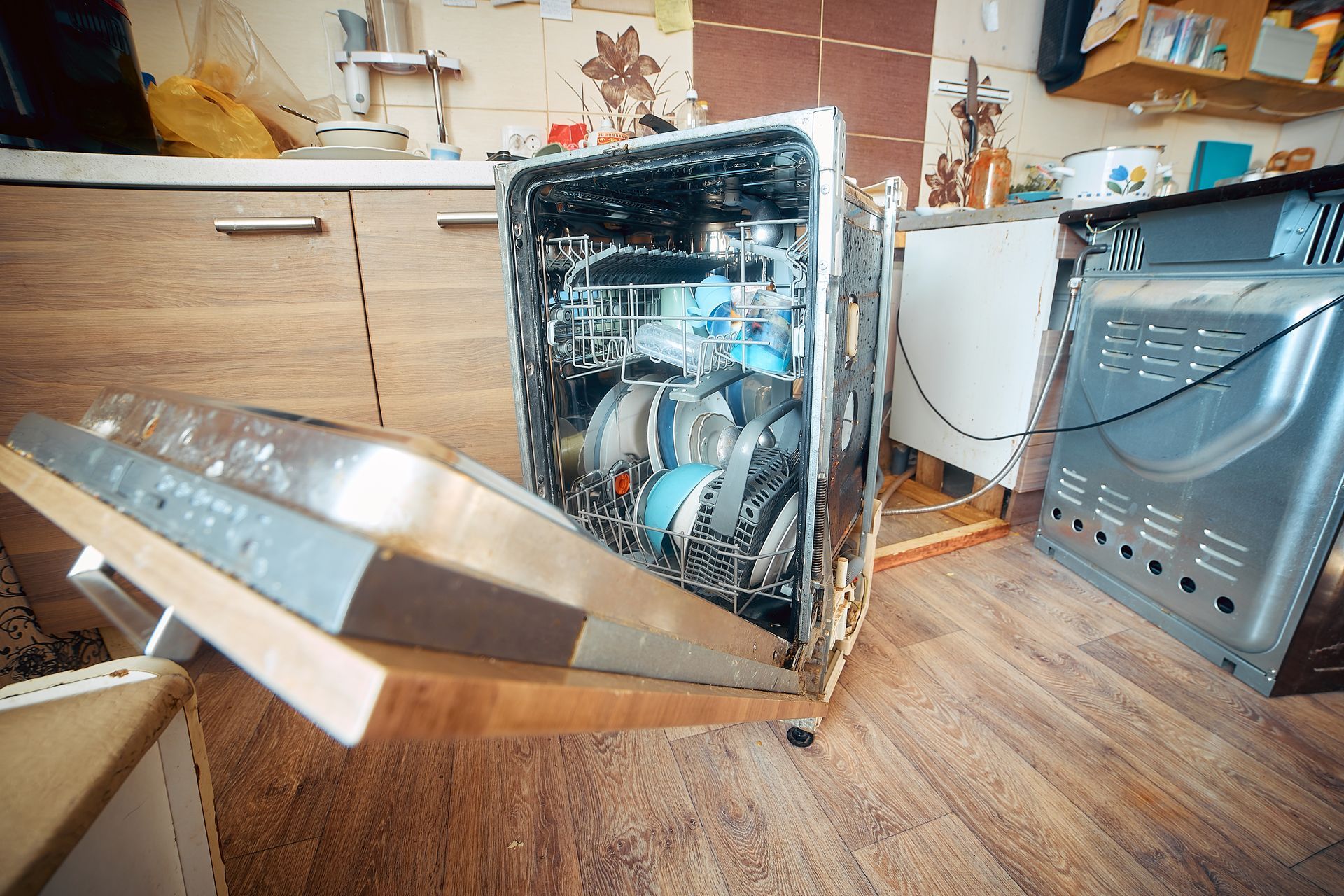Open dishwasher in a kitchen with dishes inside and the lower rack pulled out on the floor