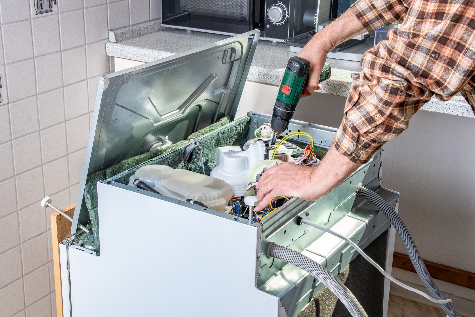 Person repairing an open washing machine in a tiled utility room