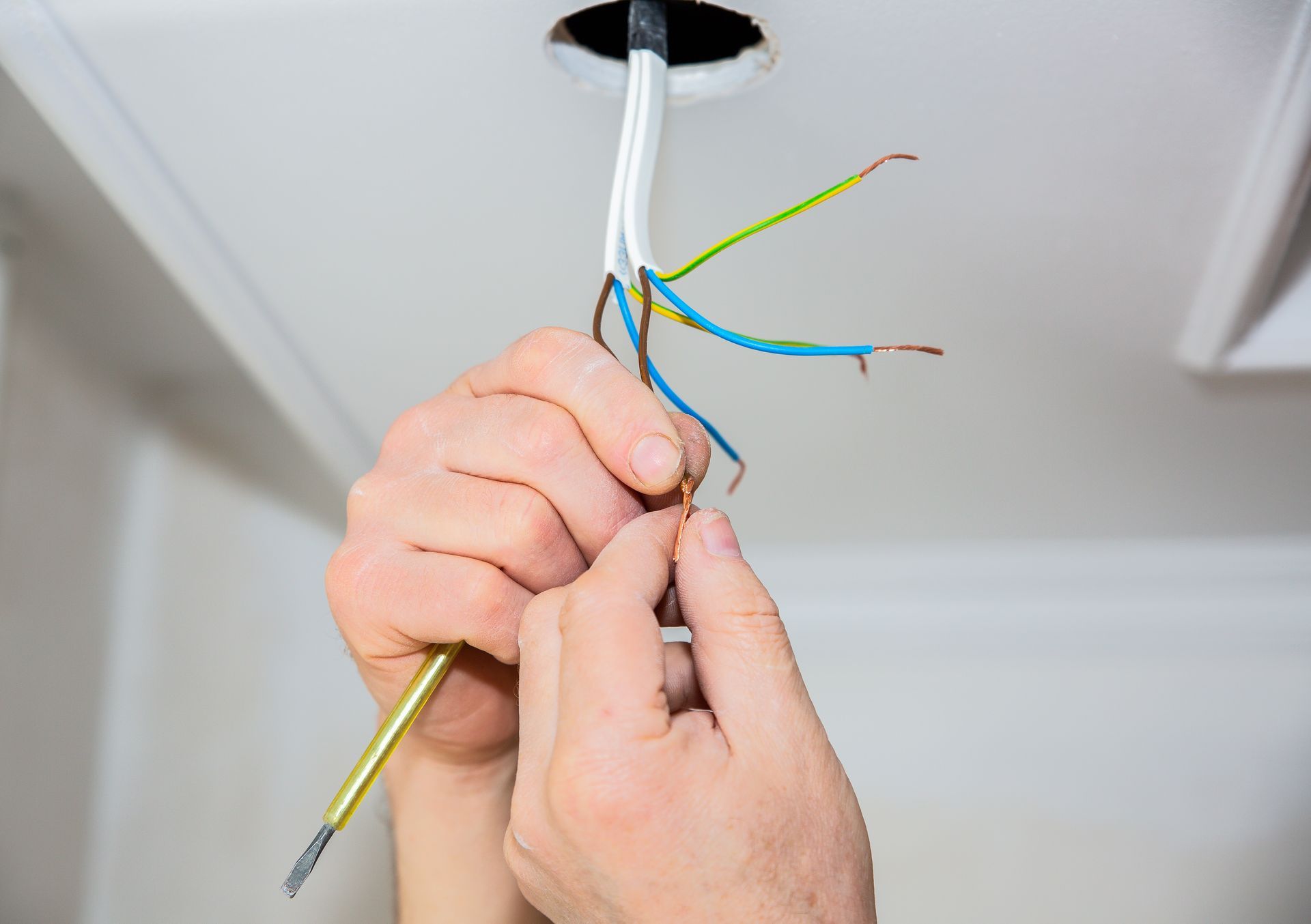 Hands wiring ceiling light fixture with exposed colored electrical wires