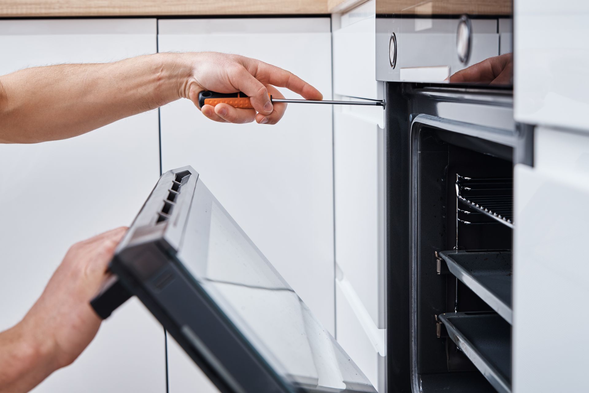 Person placing a tray into a built-in kitchen oven while another hand points at the controls