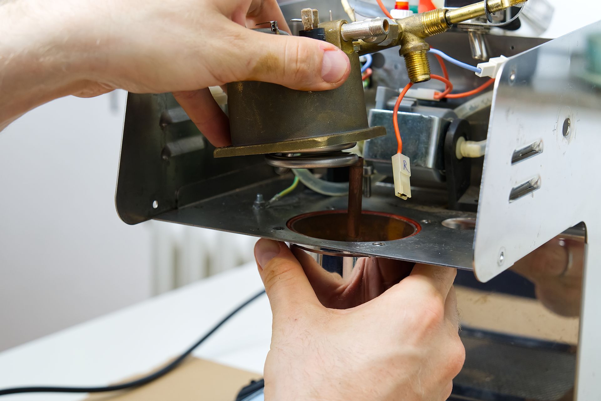 Hands adjusting espresso machine parts over a drip tray, with coffee dripping into a cup below