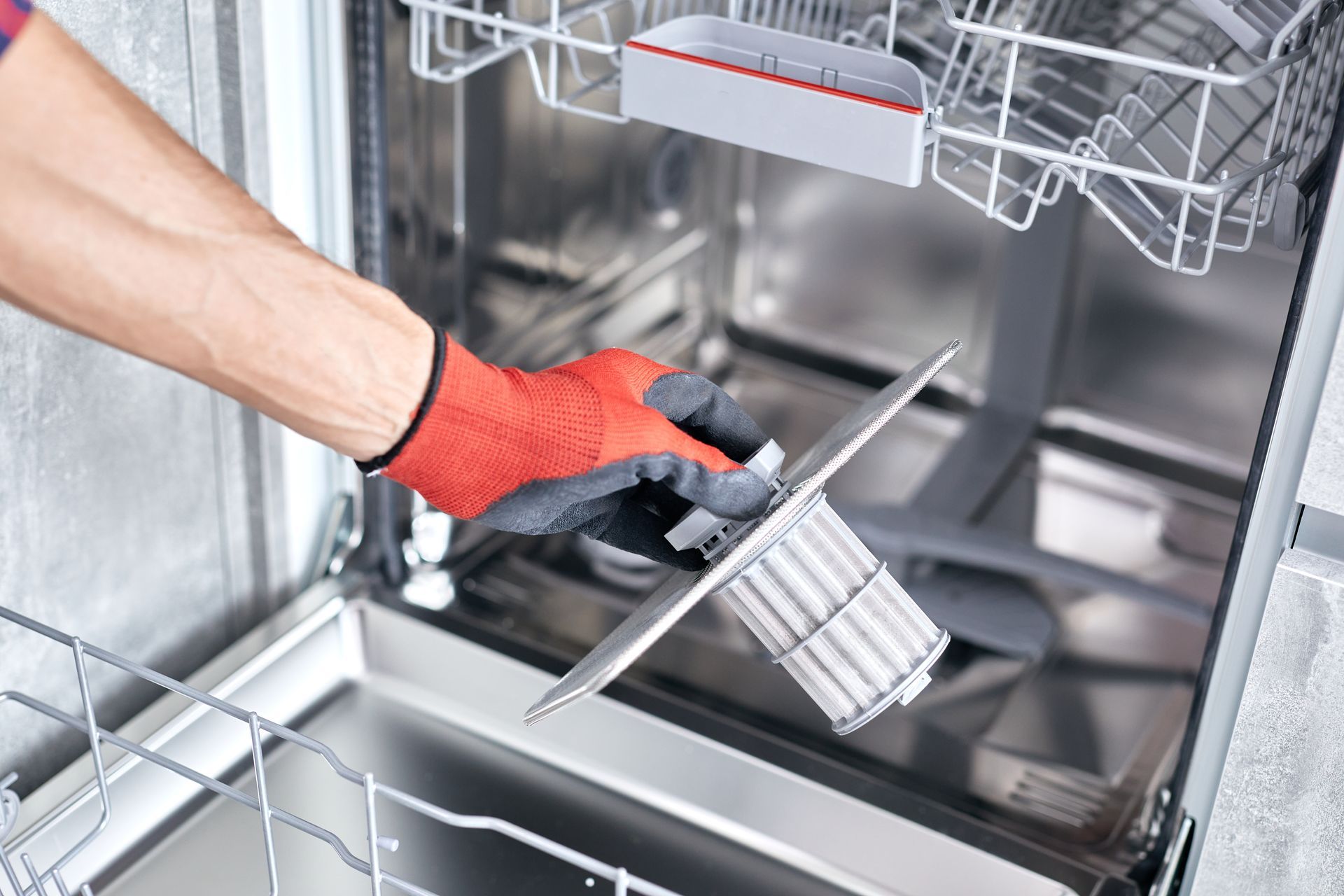 Gloved hand loading a dishwasher rack with a metal utensil basket