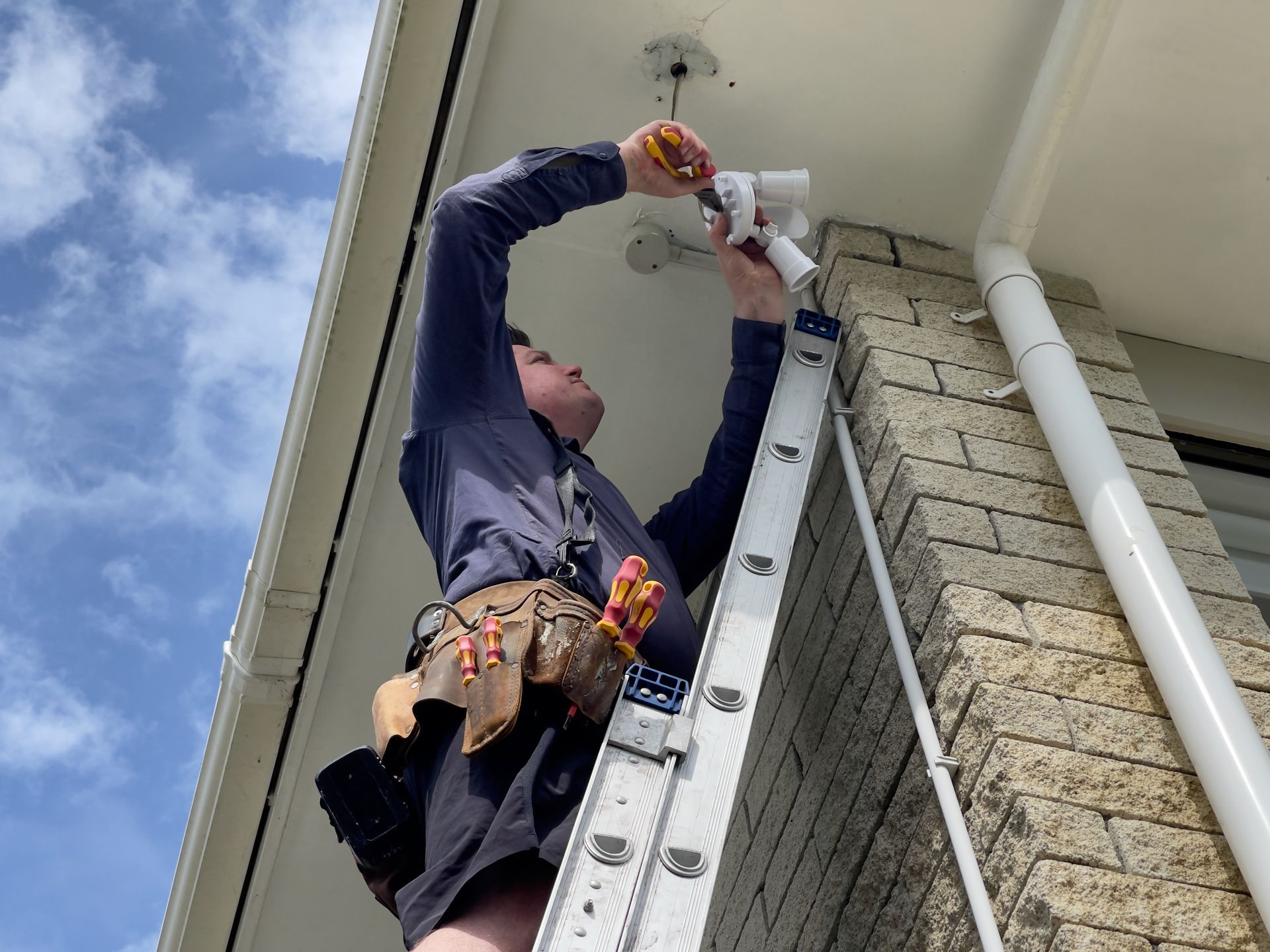 Worker on a ladder repairing the roof gutter beside a brick house
