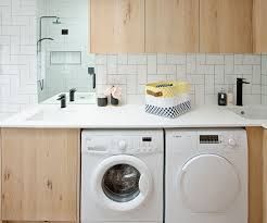 Modern laundry room with white sink, wood cabinets, tiled backsplash, and washer-dryer under countertop