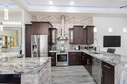 Modern kitchen with dark wood cabinets, stainless steel appliances, granite counters, and stone backsplash