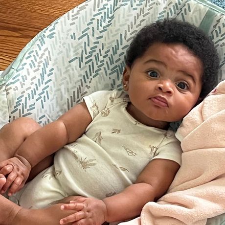 A baby is laying on a blanket in a bouncer.