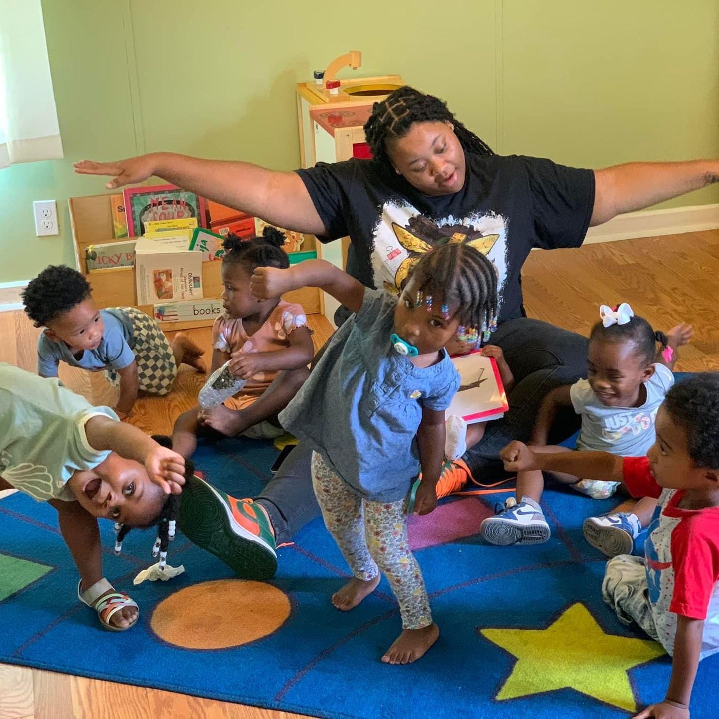 A group of children are playing on a blue rug in a room.