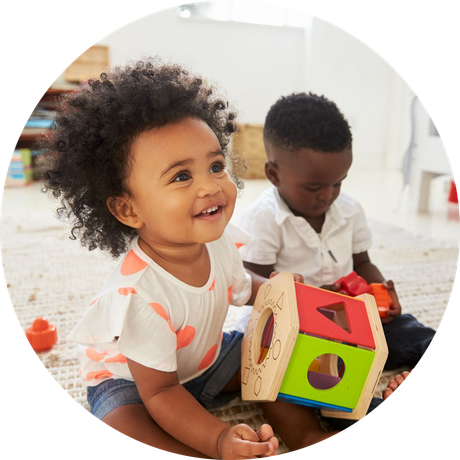 Two babies are sitting on the floor playing with toys.