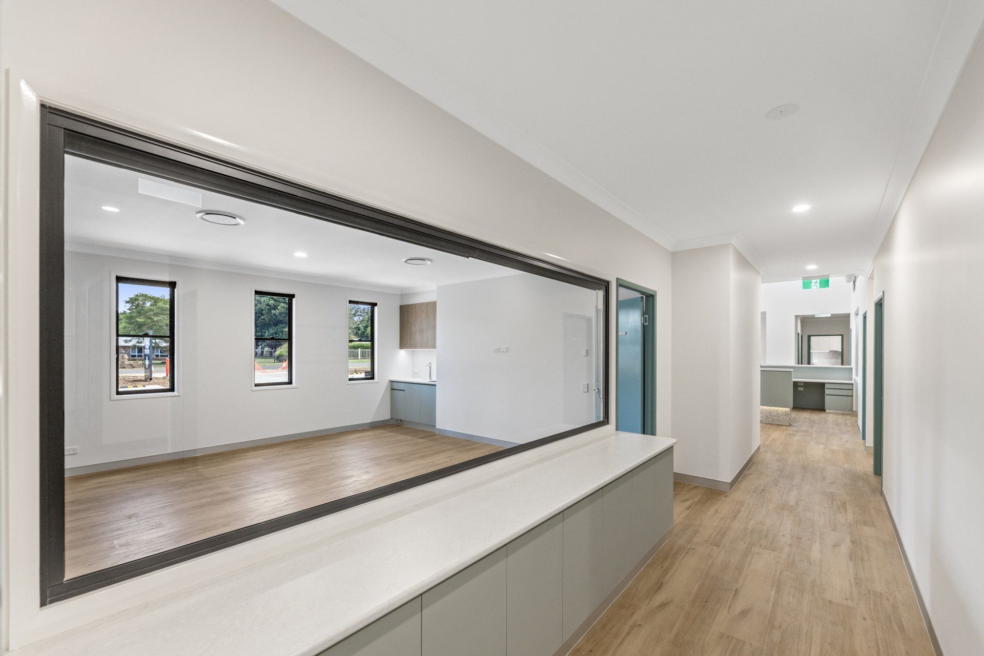 Bright modern hallway with wood floors and large interior window opening into an empty room