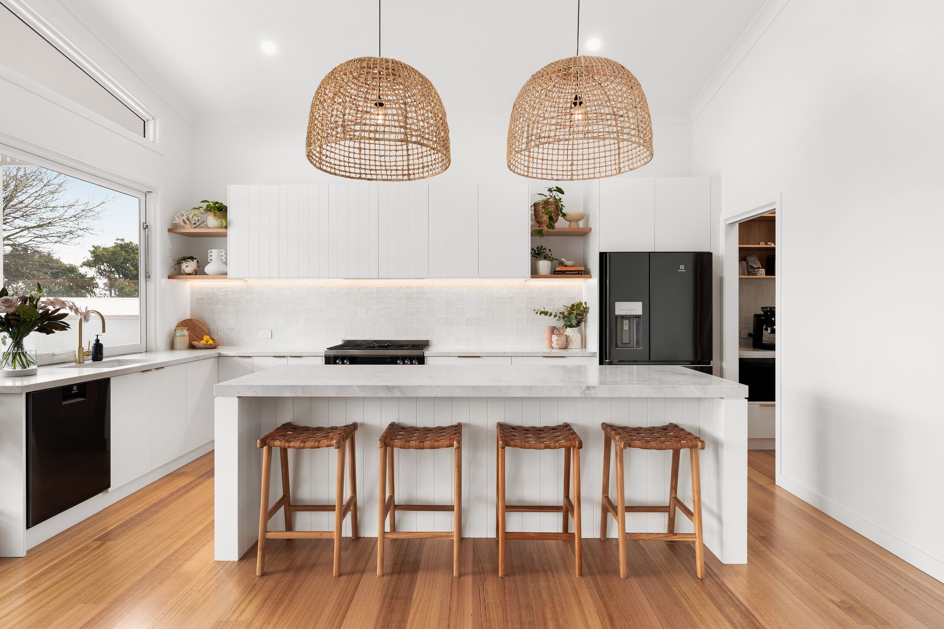 Bright modern kitchen with white cabinetry, wood floors, island stools, and woven pendant lights