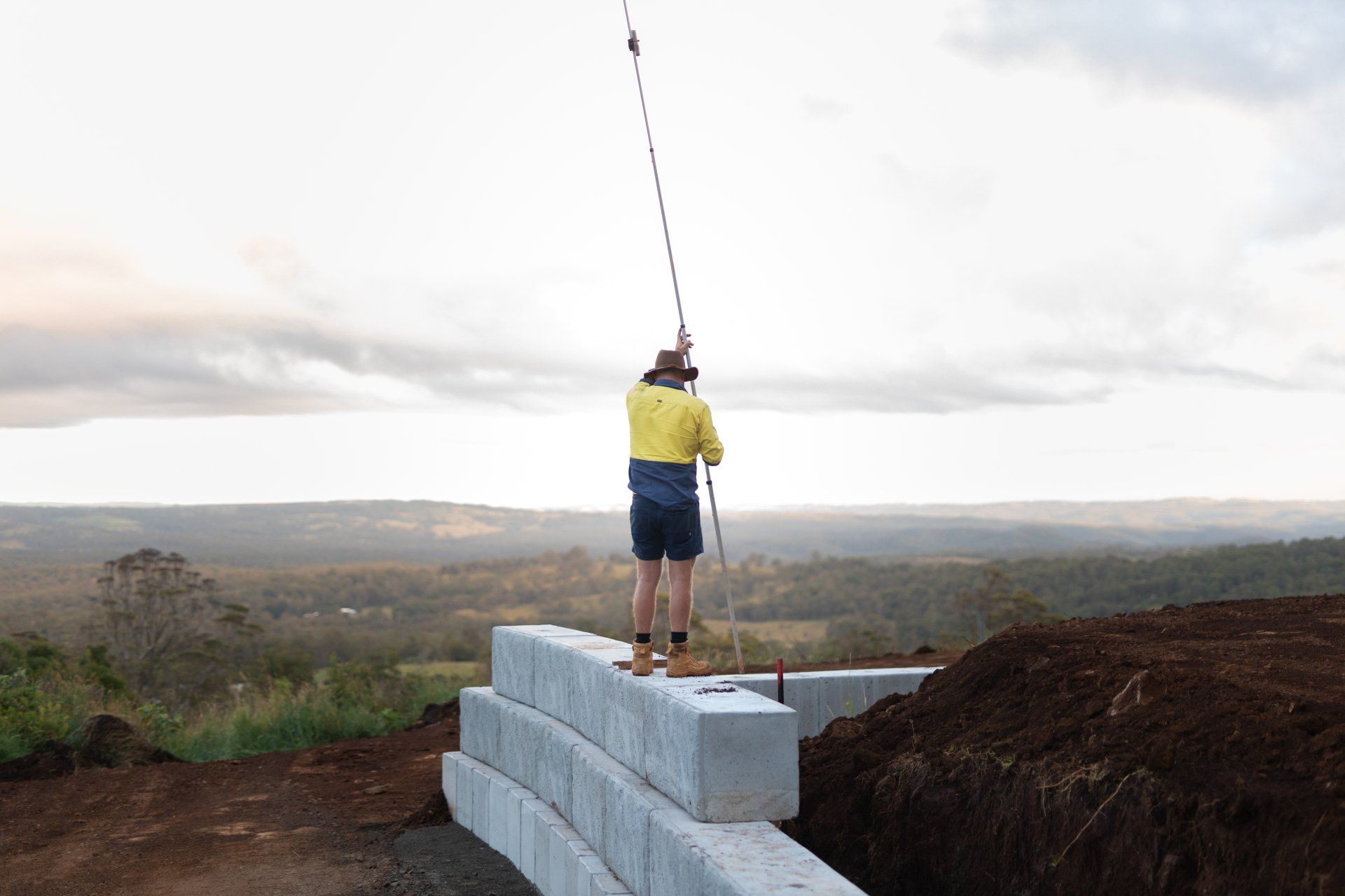 Person fishing from a concrete ledge overlooking a wide landscape at sunset