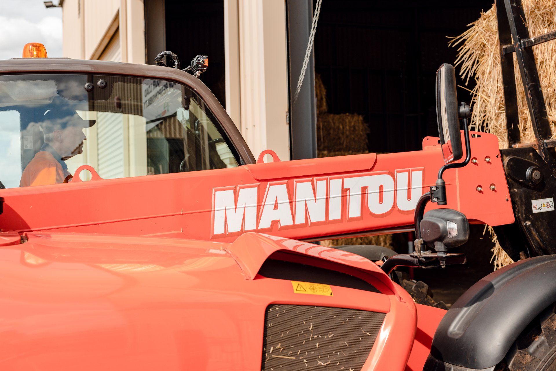Red Manitou forklift parked beside a barn, with a black tire and open cab visible