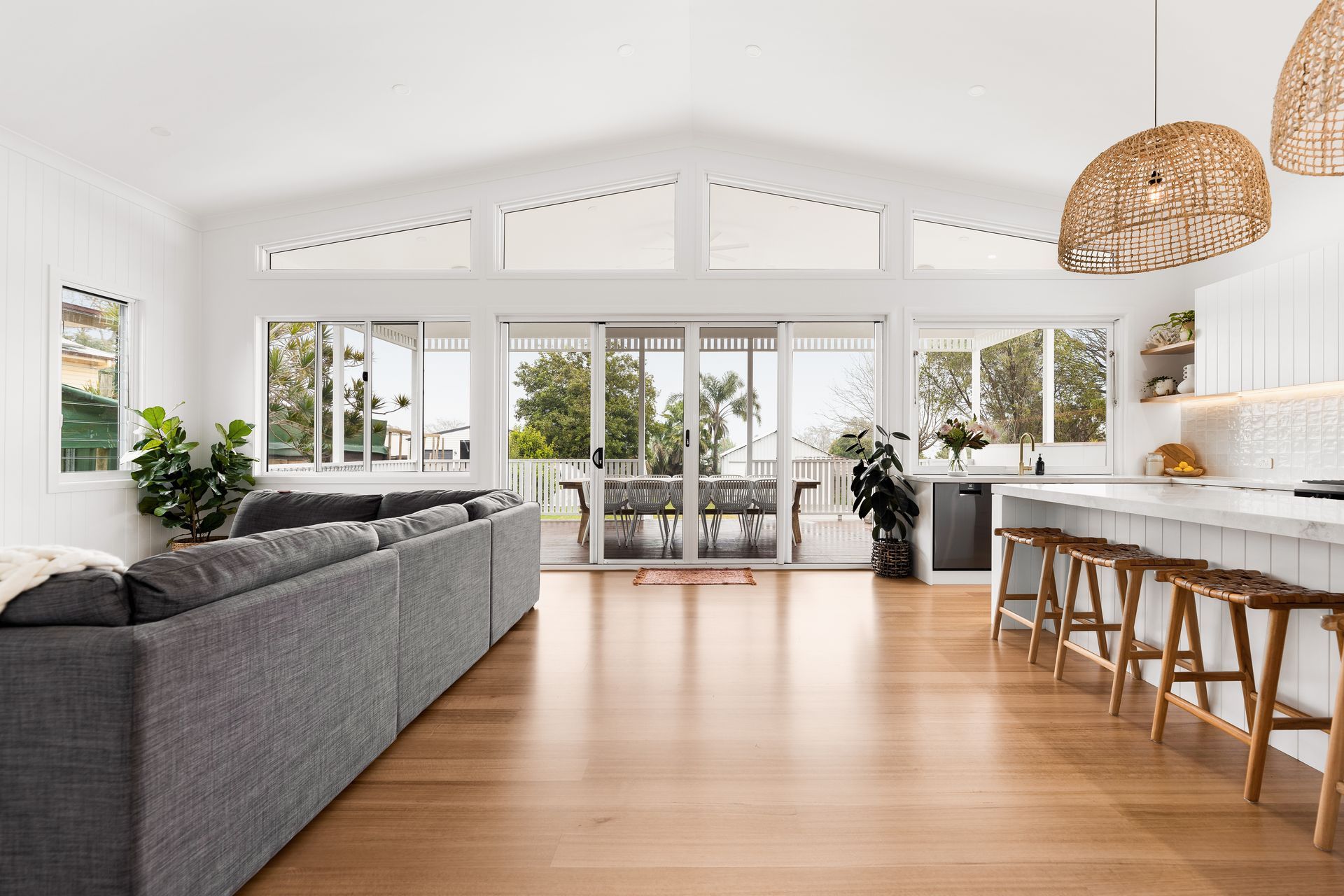 Bright open living room with gray sofa, wood floor, bar stools, and large windows opening to a patio