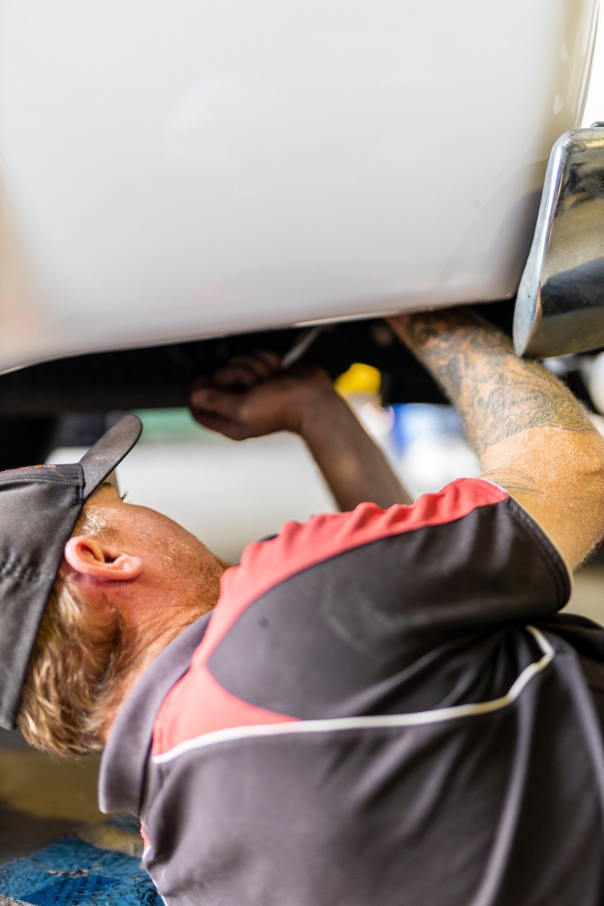 Mechanic working under a vehicle, reaching up with a tool near the undercarriage