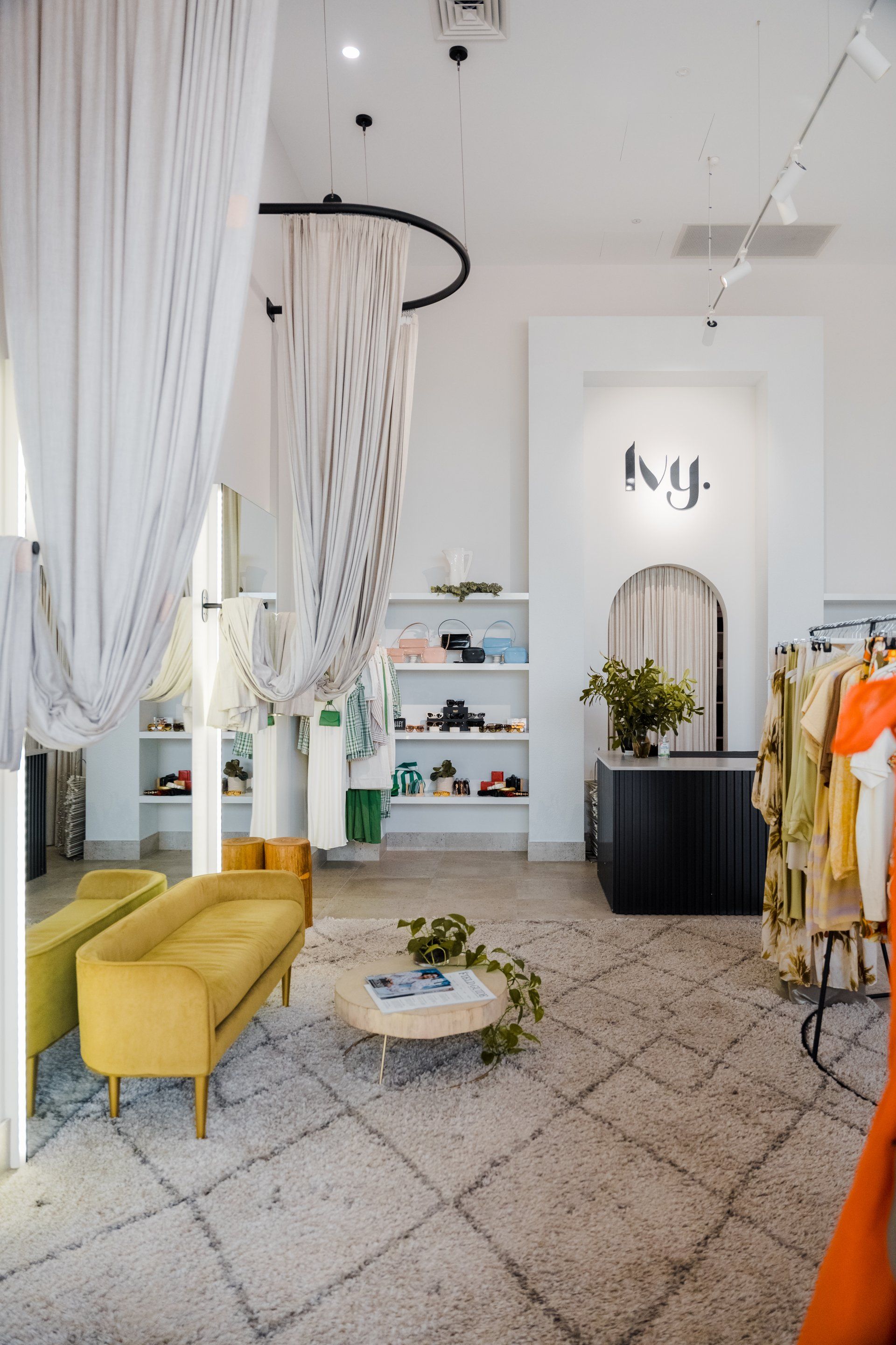 Bright boutique interior with white curtains, yellow sofa, clothing racks, and a mirror display