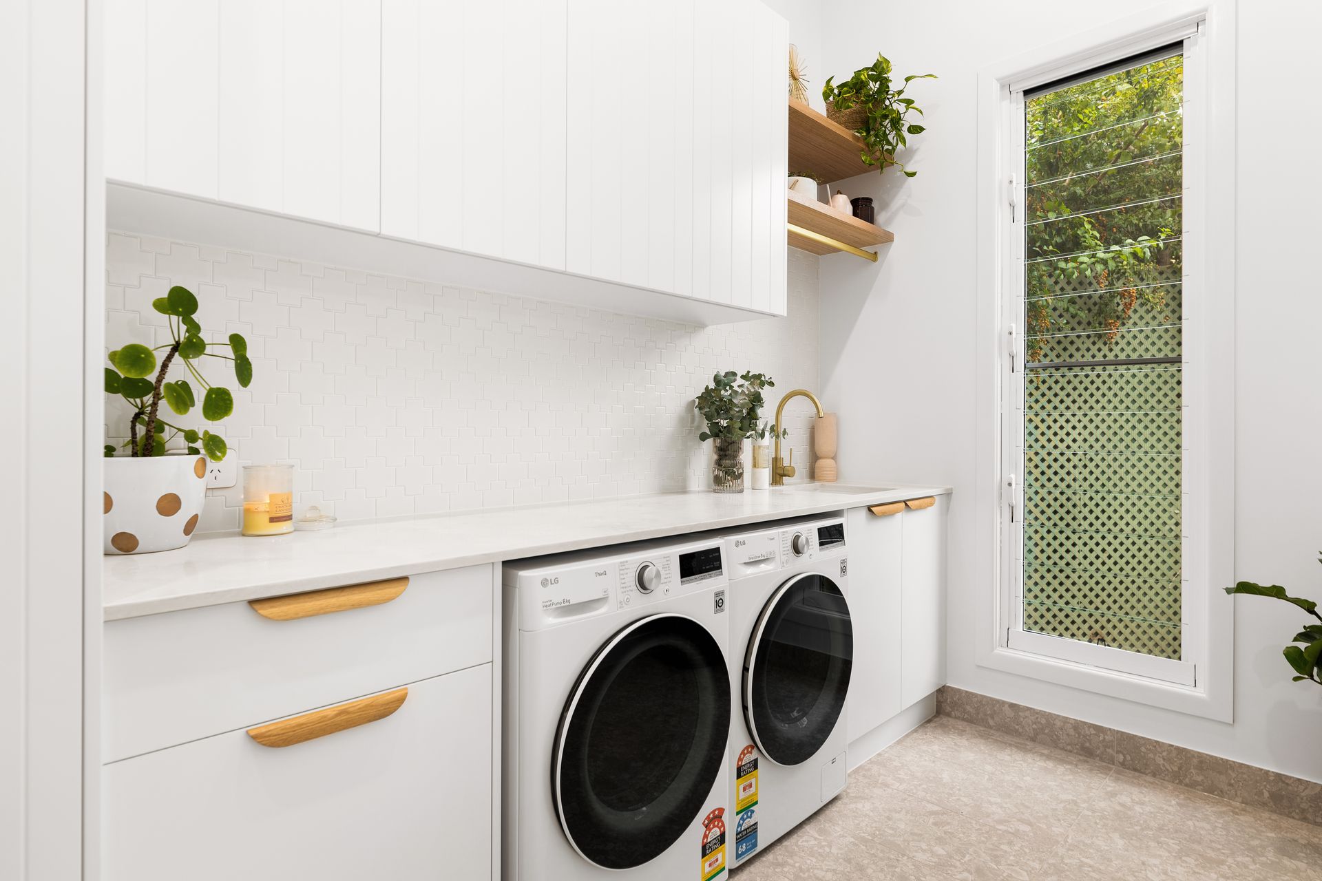 Bright laundry room with stacked washer and dryer, white cabinets, and a glass door to greenery