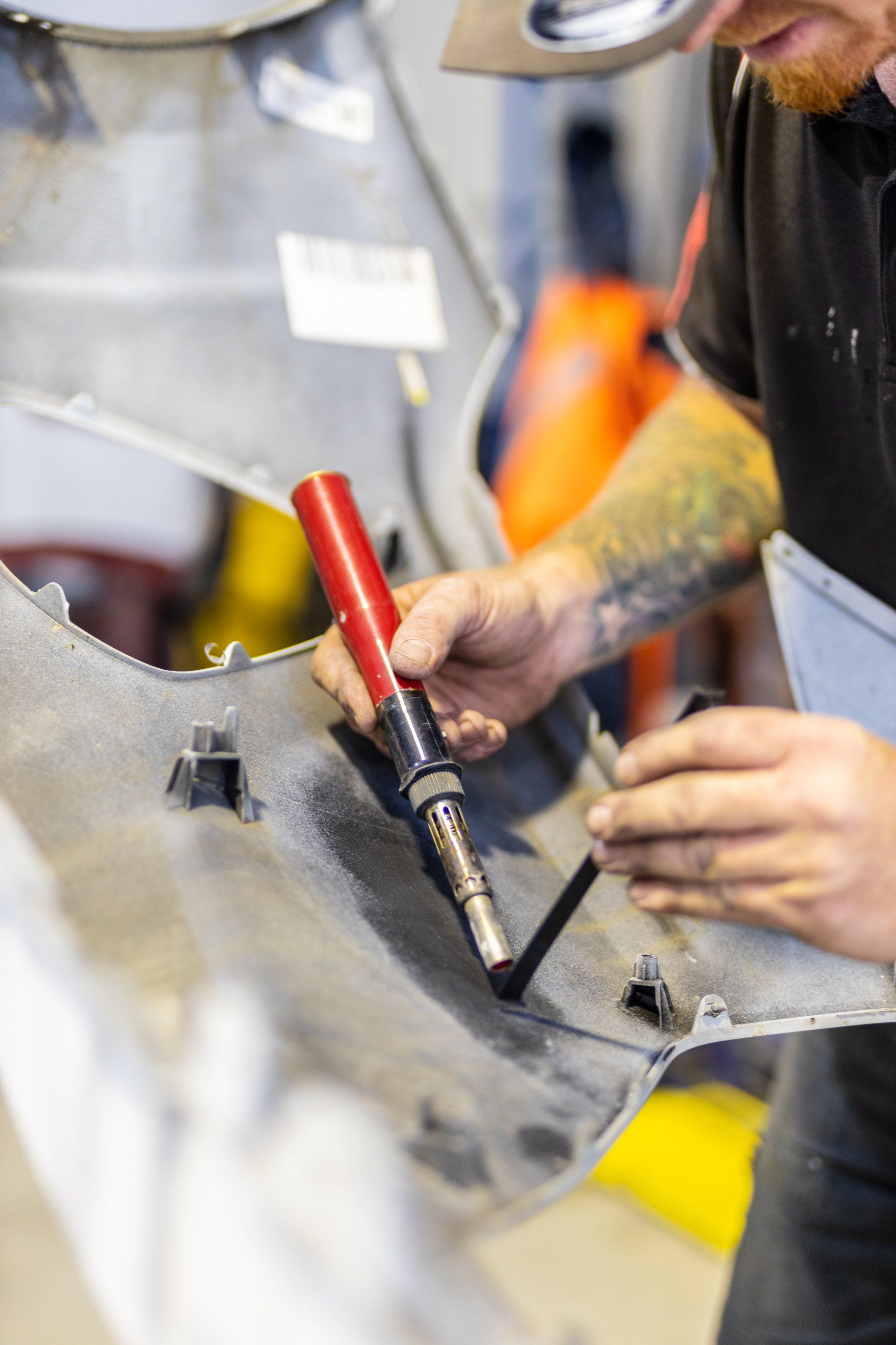 Mechanic welding a metal part with a red-handled torch in a workshop