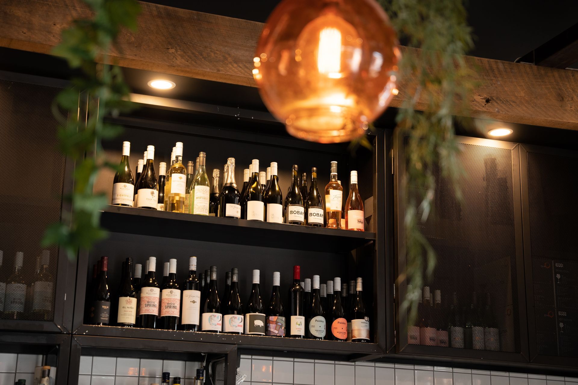 Backlit wine bottles on shelves in a cozy bar, with a warm hanging lamp in the foreground