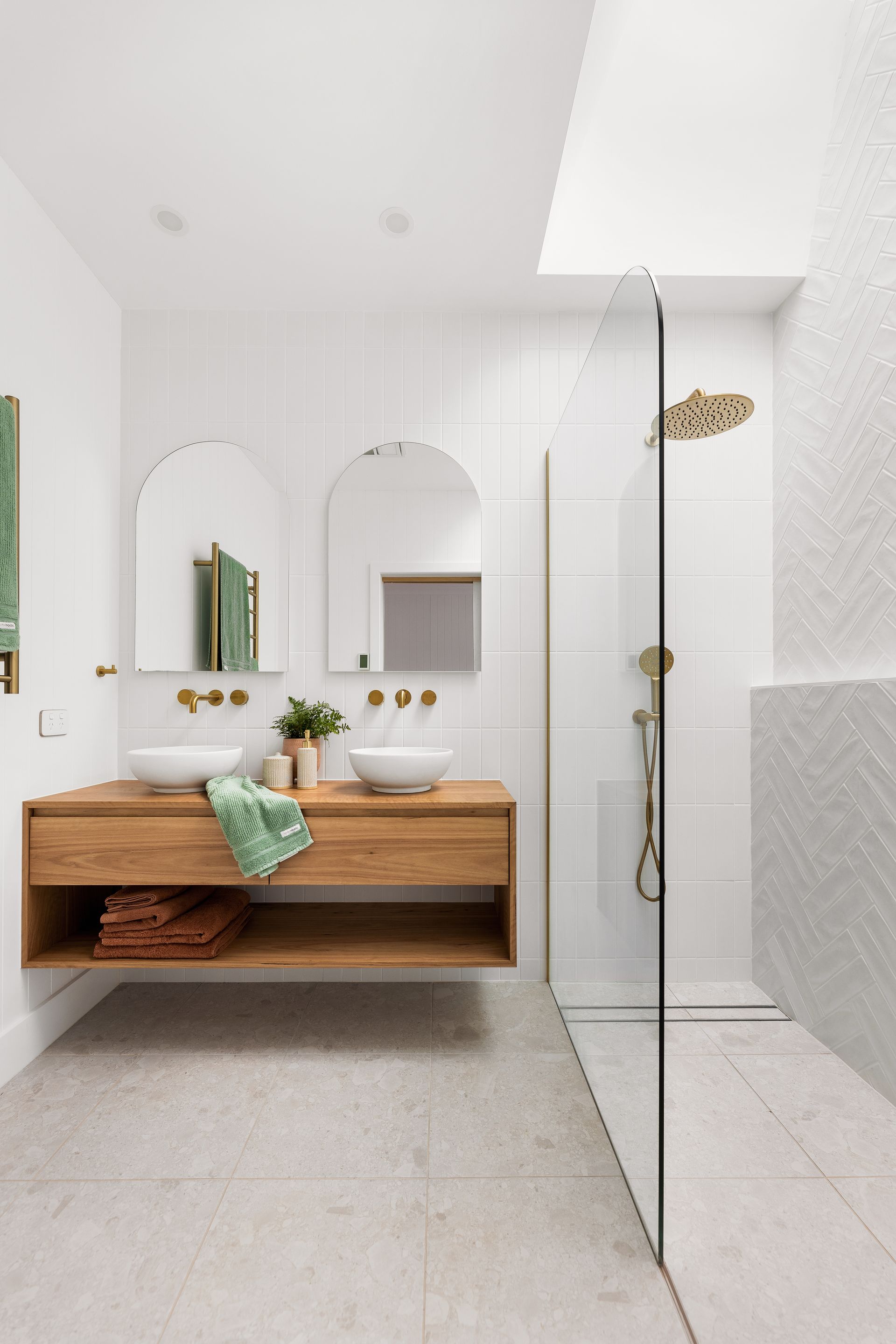Bright white bathroom with wooden vanity, arched mirrors, and a glass shower enclosure