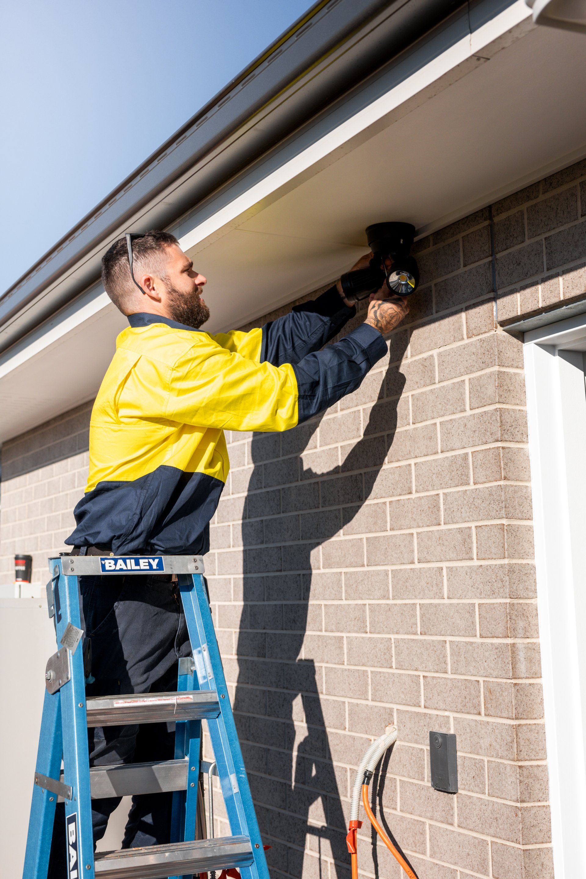 Worker on a ladder using a power tool to repair a brick wall under the roof eaves