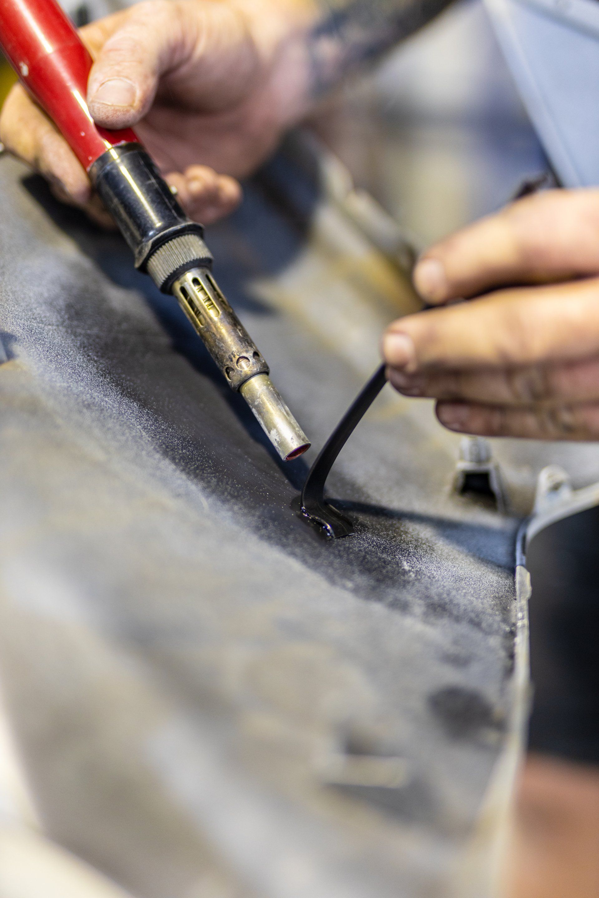 Hands soldering a black seam with a red soldering iron on a metal surface