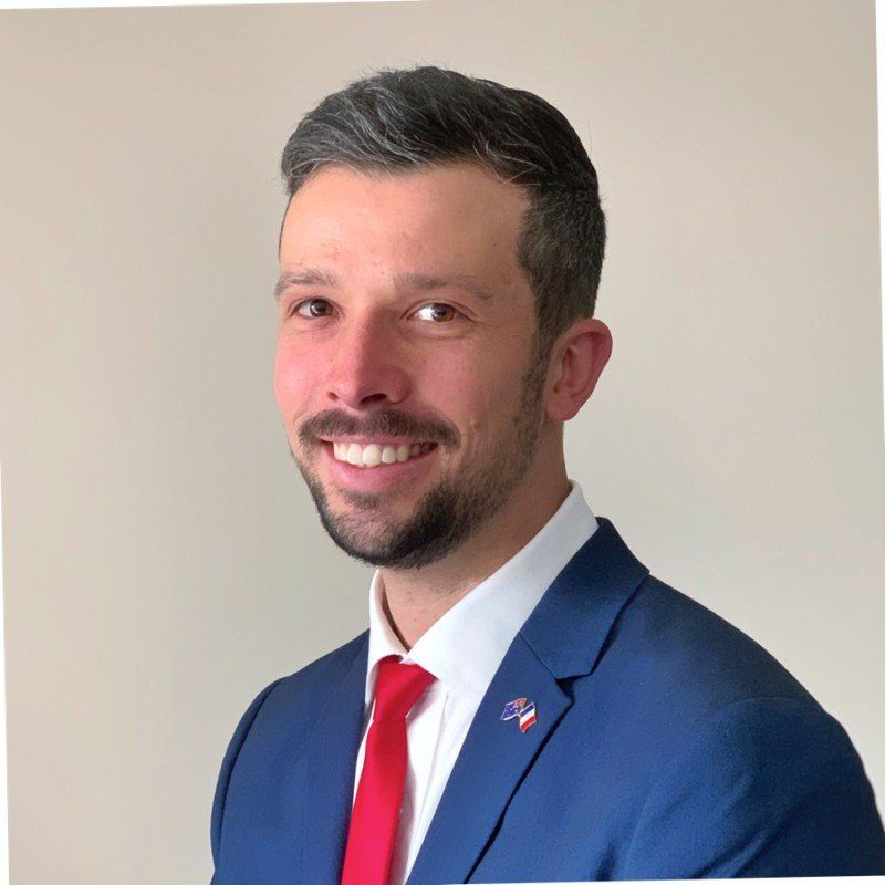 Smiling man in a blue suit and red tie against a plain beige background