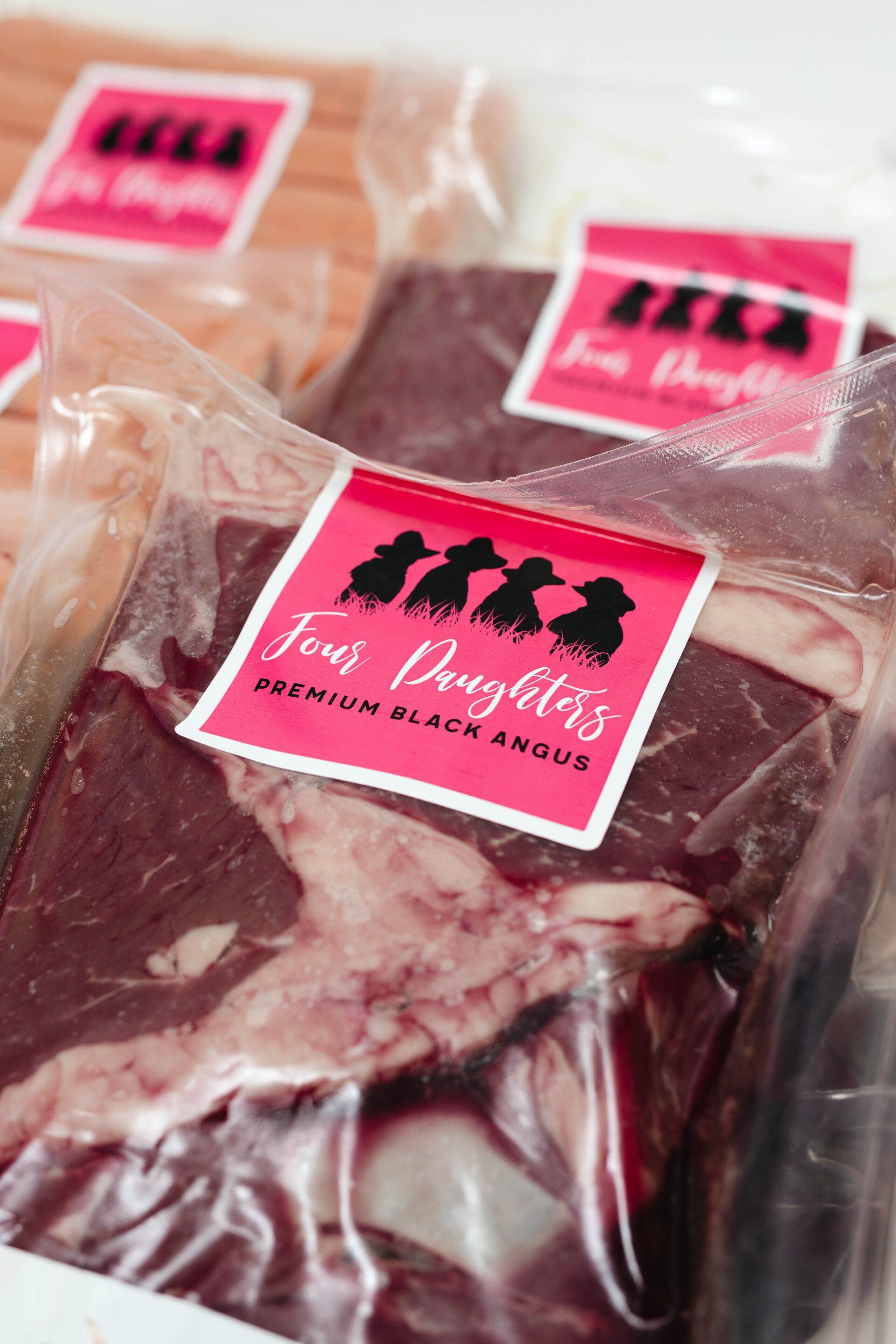 Vacuum-sealed packages of raw meat with pink labels on a store shelf