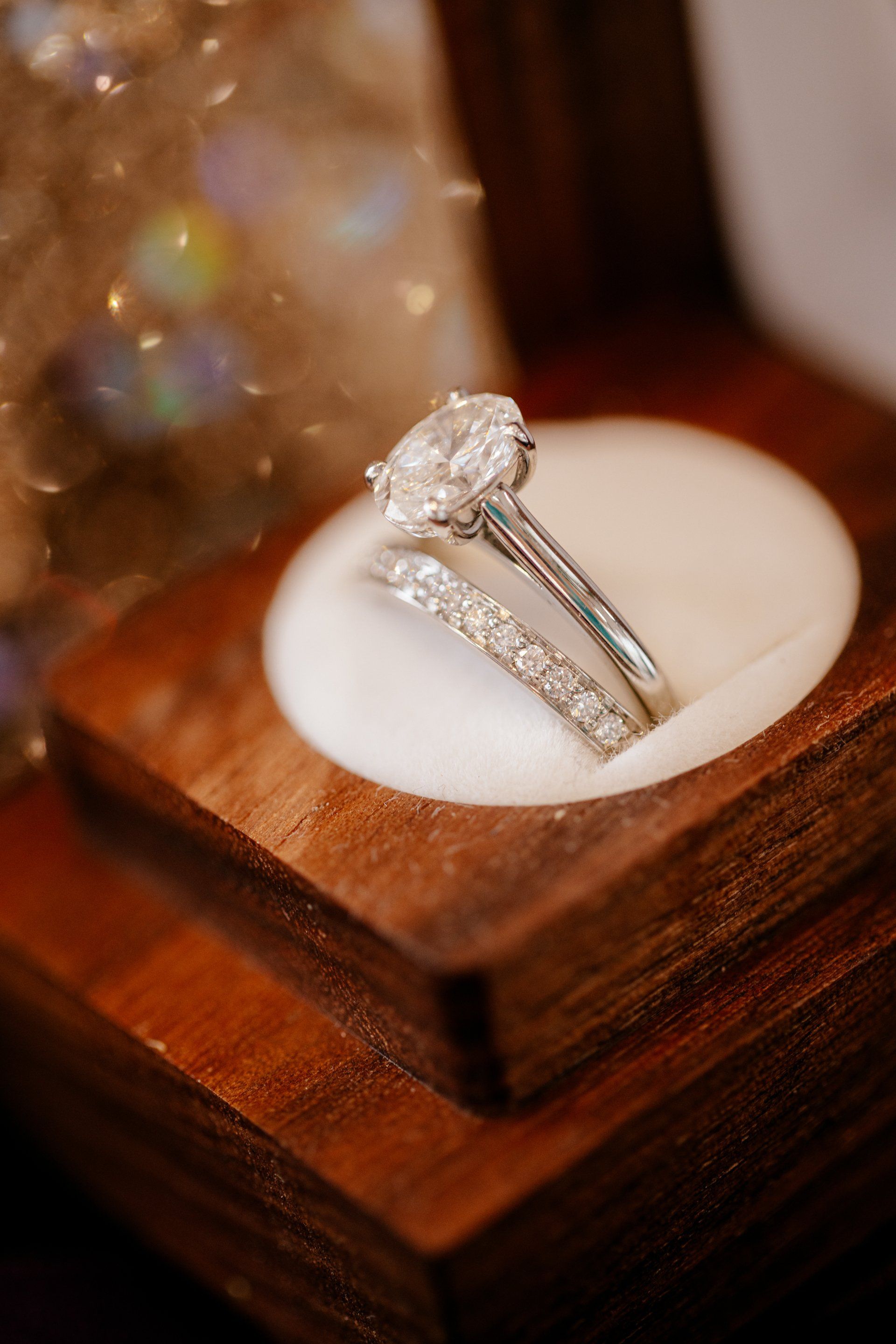 Diamond engagement ring displayed in a wooden box on a white cushion