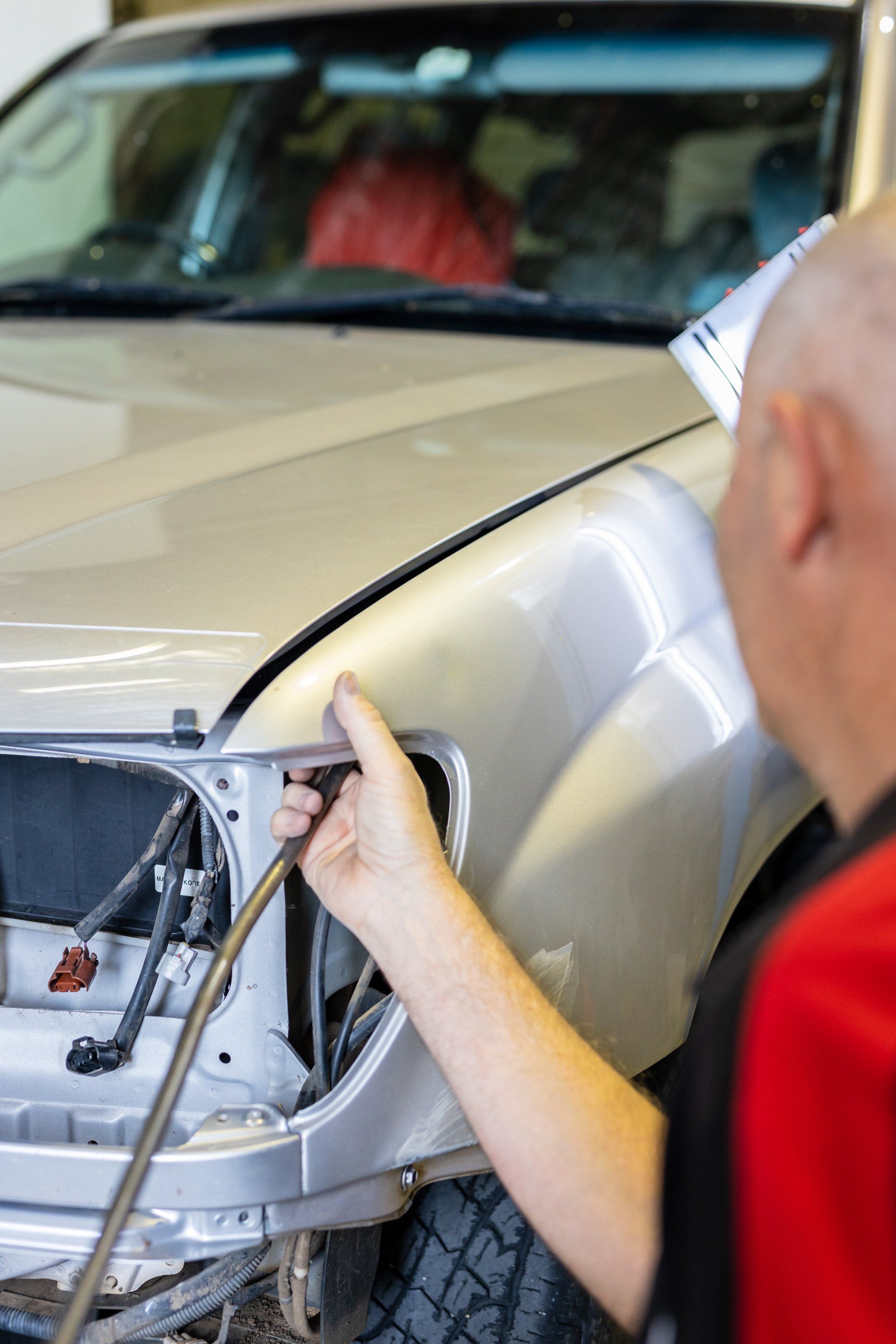 Person working on the front of a beige car in a garage, removing the headlight area.