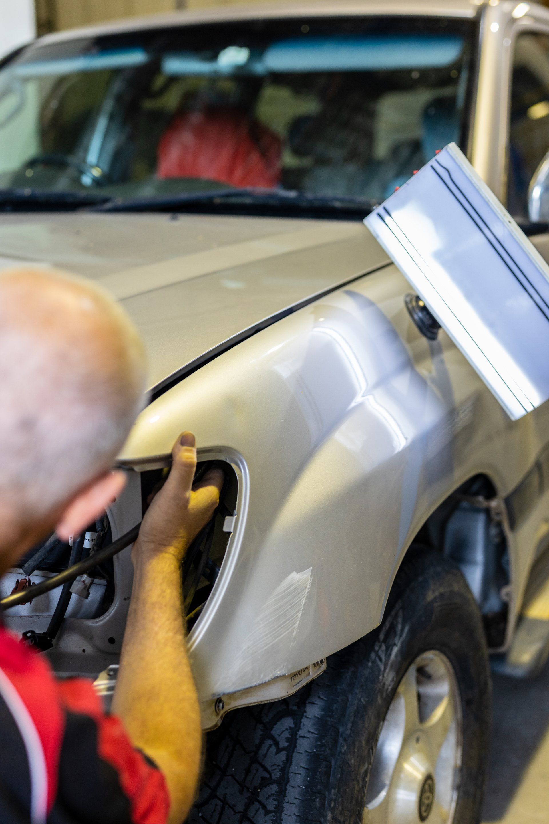 Worker sanding a beige car fender with a tool in a garage