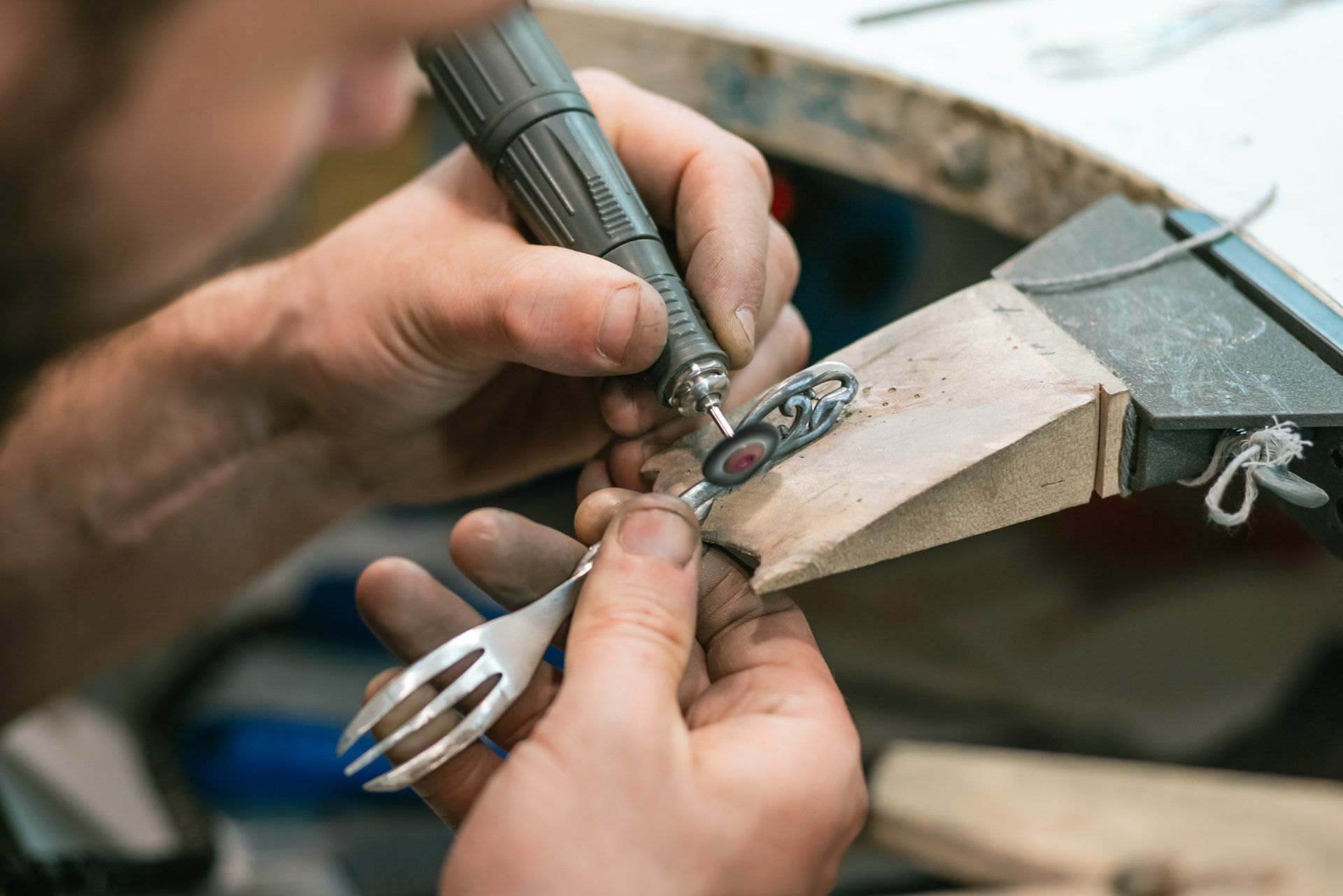 Hands use a rotary tool to engrave a small metal piece on a workbench.