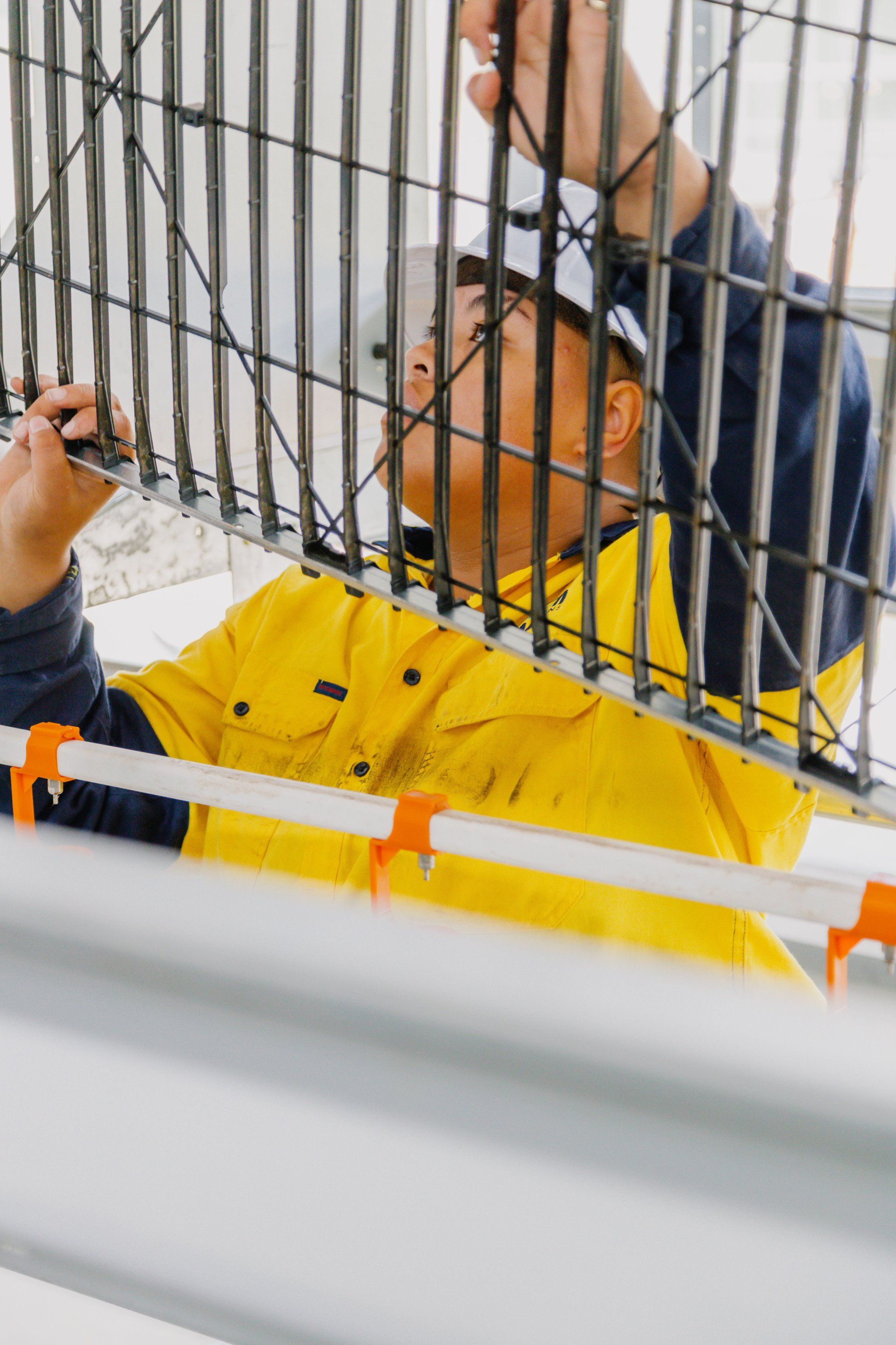 Person in a yellow jacket standing behind metal bars, looking up and touching the cage.