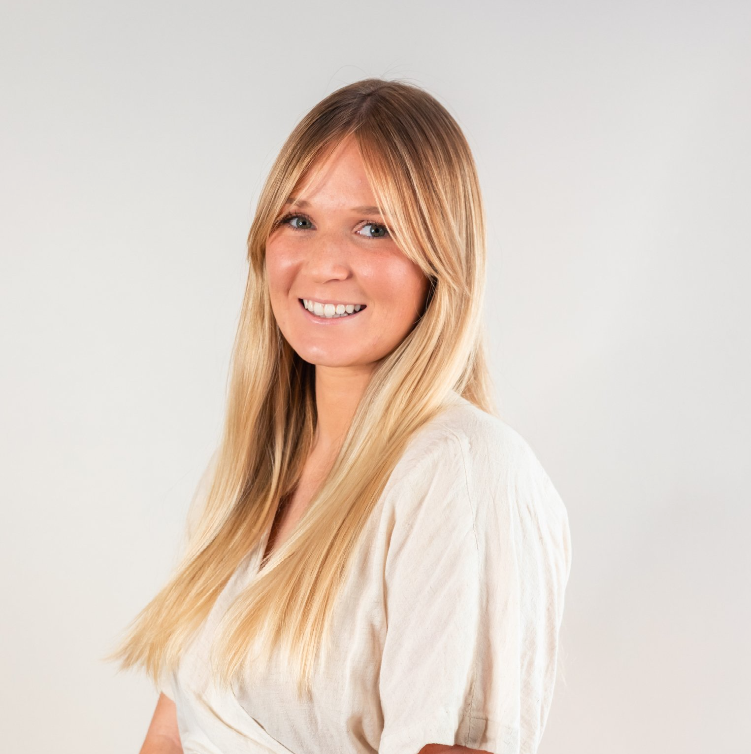 Smiling blonde woman in a white top against a light gray background