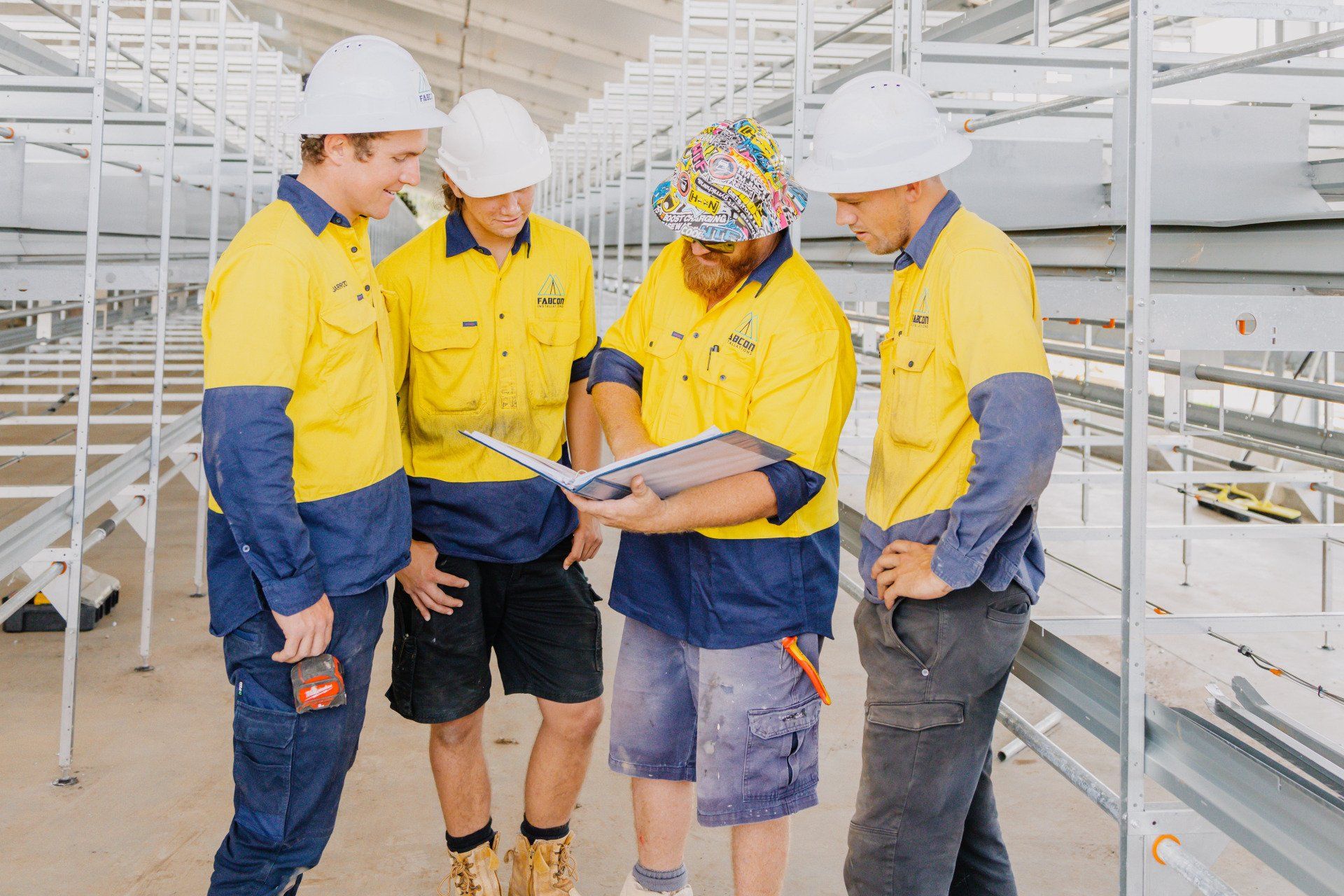 Workers in yellow safety gear reviewing a clipboard in an industrial facility