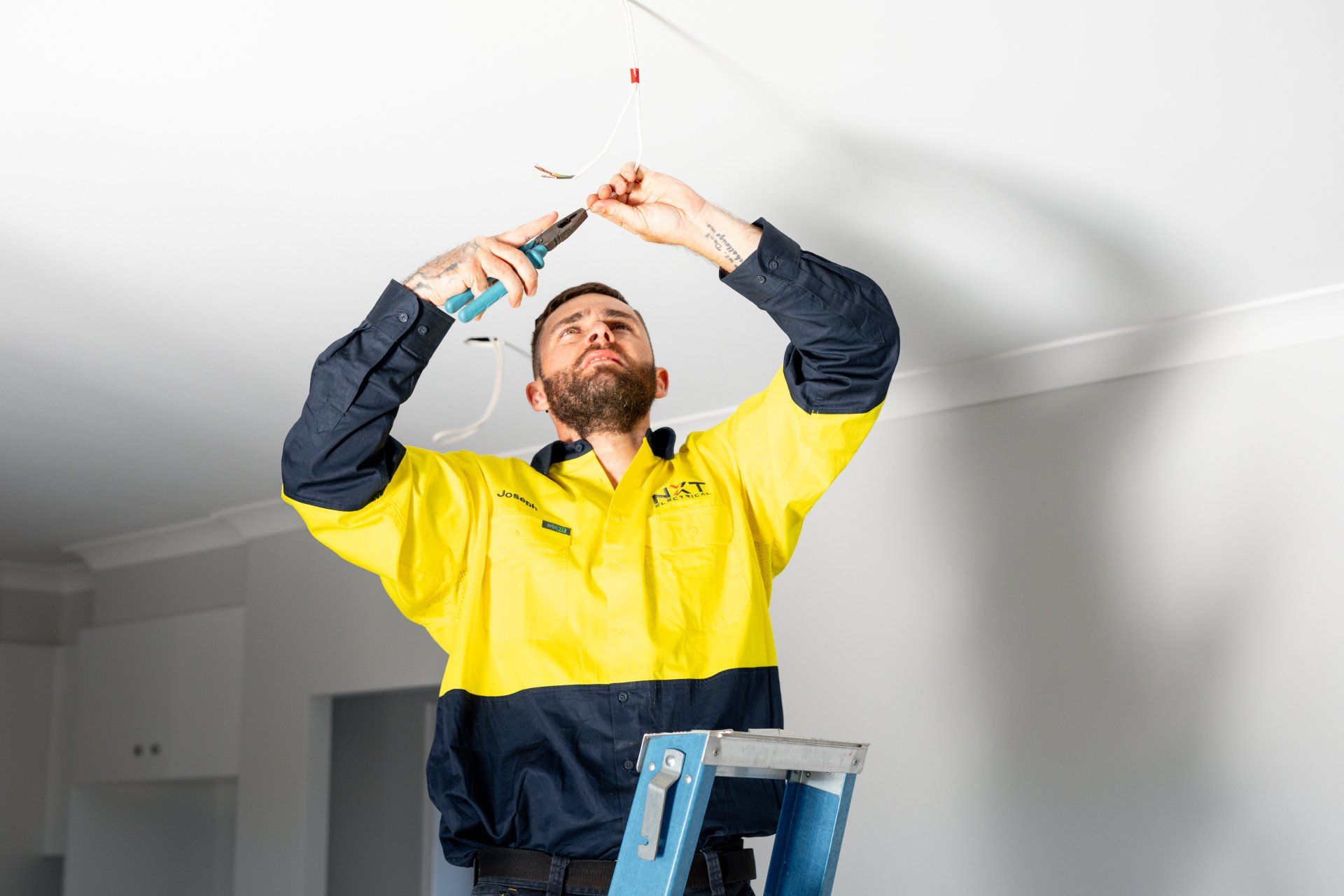 Worker in yellow jacket painting a ceiling near a blue ladder