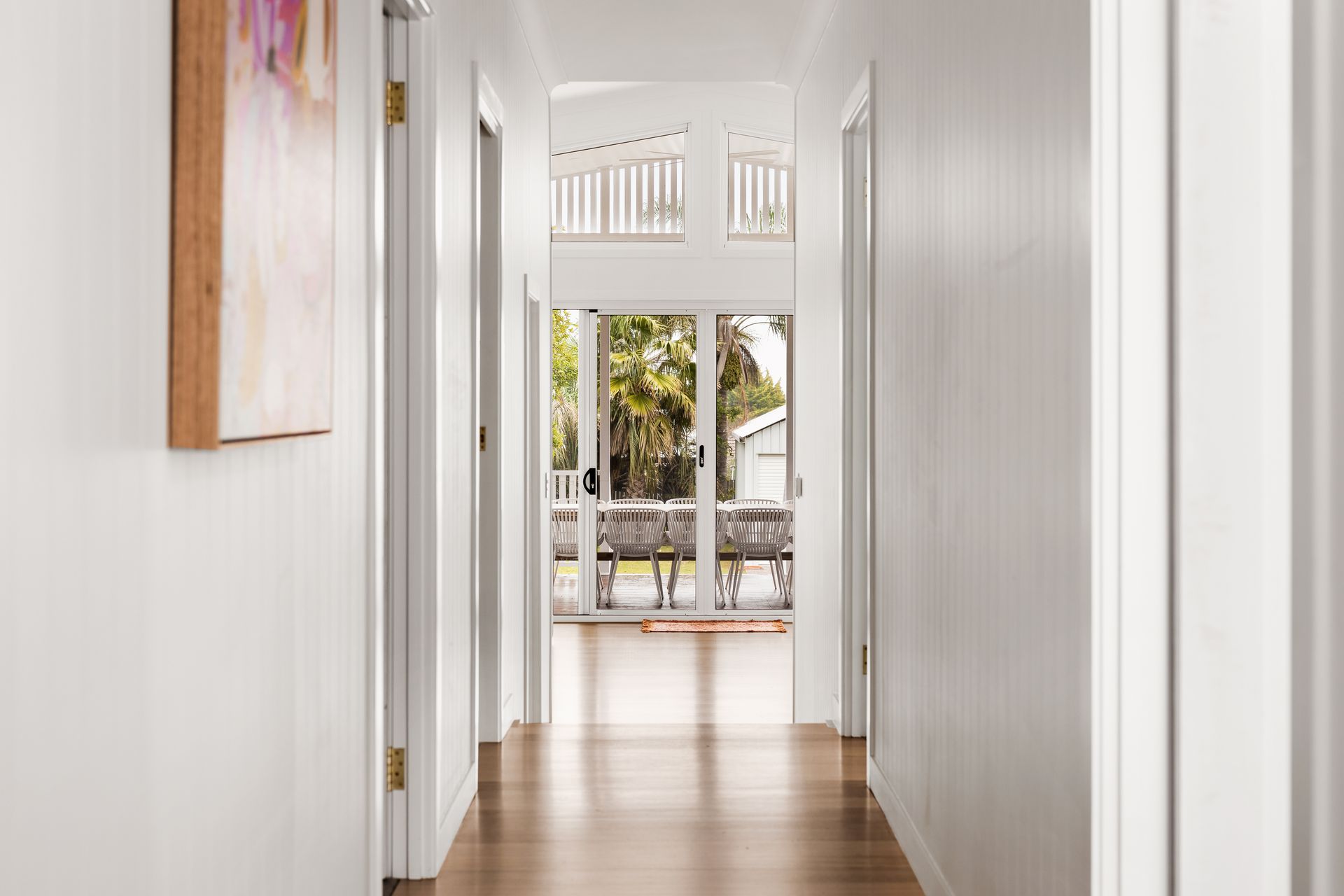 Bright hallway with white walls and wooden floor leading to a sunlit patio and garden view
