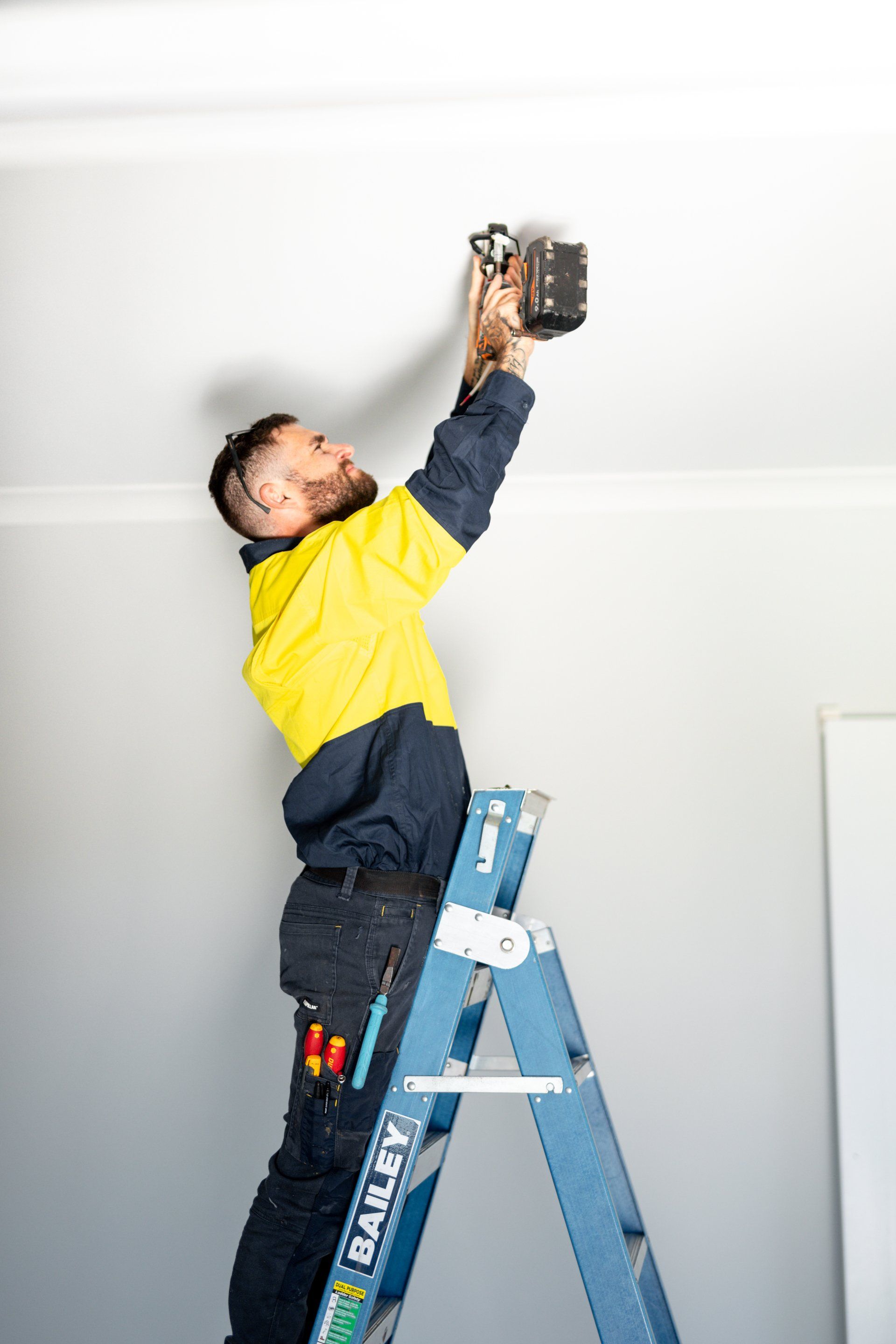 Person on a blue ladder reaching up to repair the ceiling in a white room