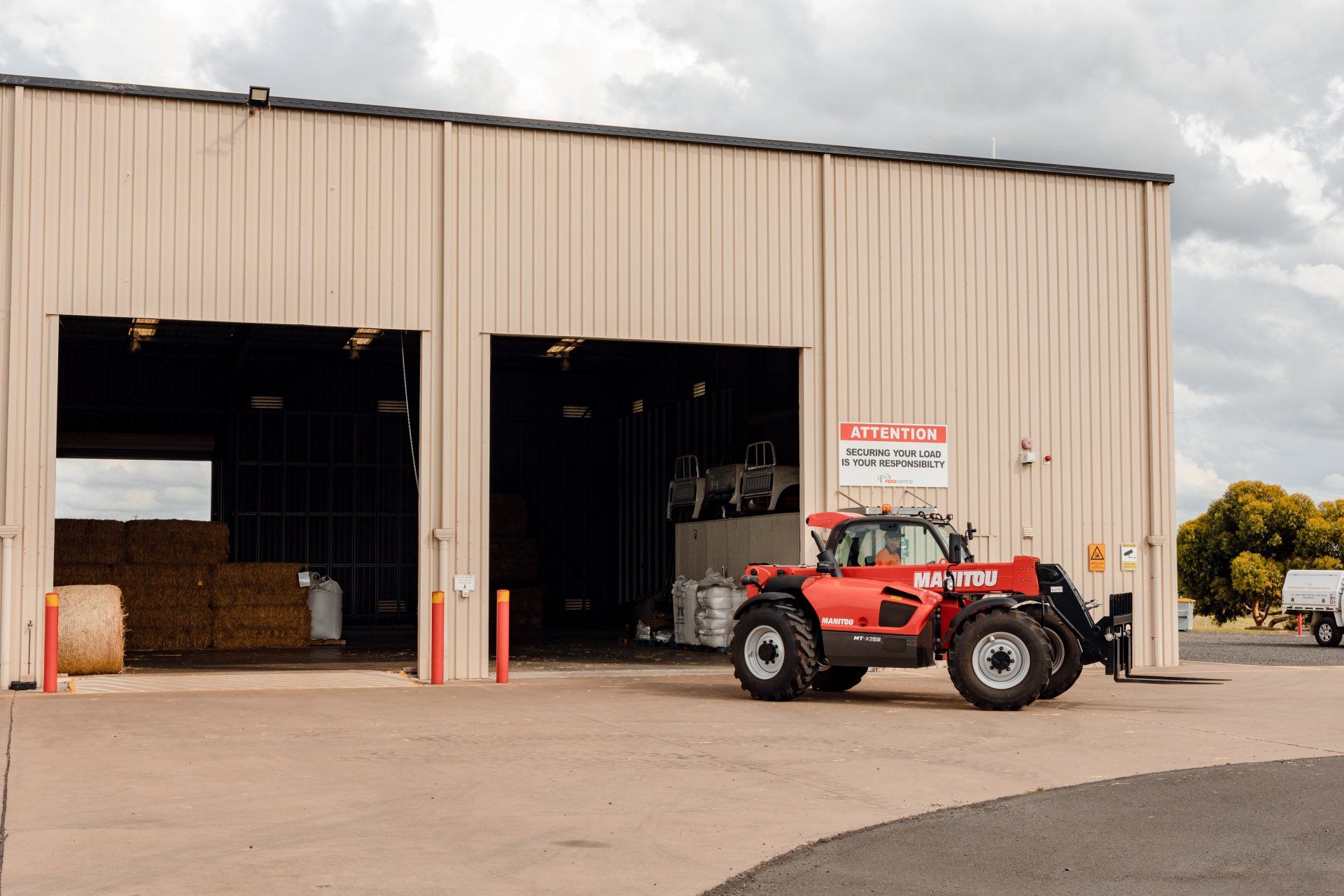 Red tractor parked outside a beige metal warehouse with open garage bays