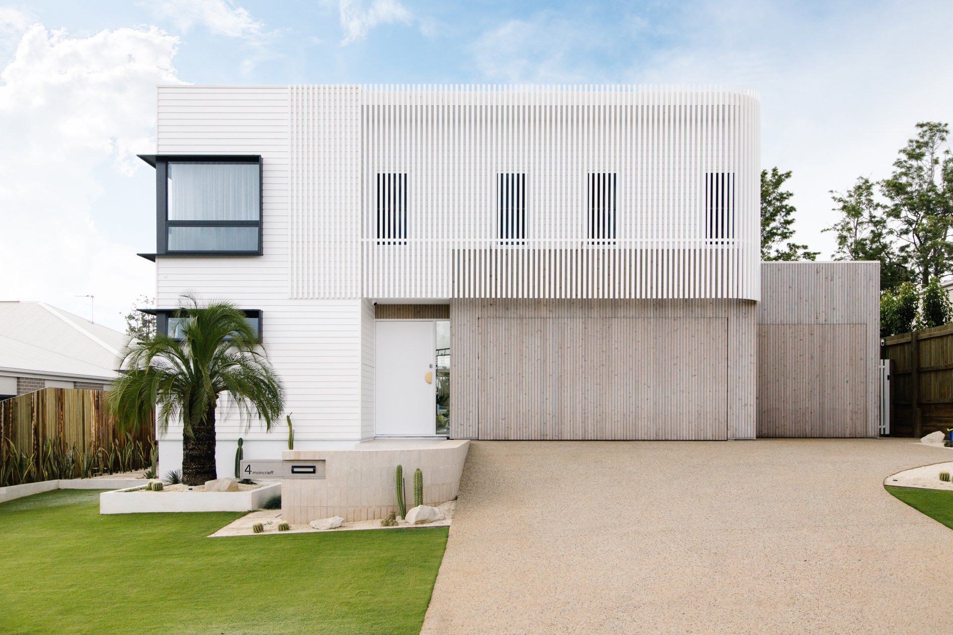 Modern white two-story house with vertical slats, garage, palm tree, and gravel driveway