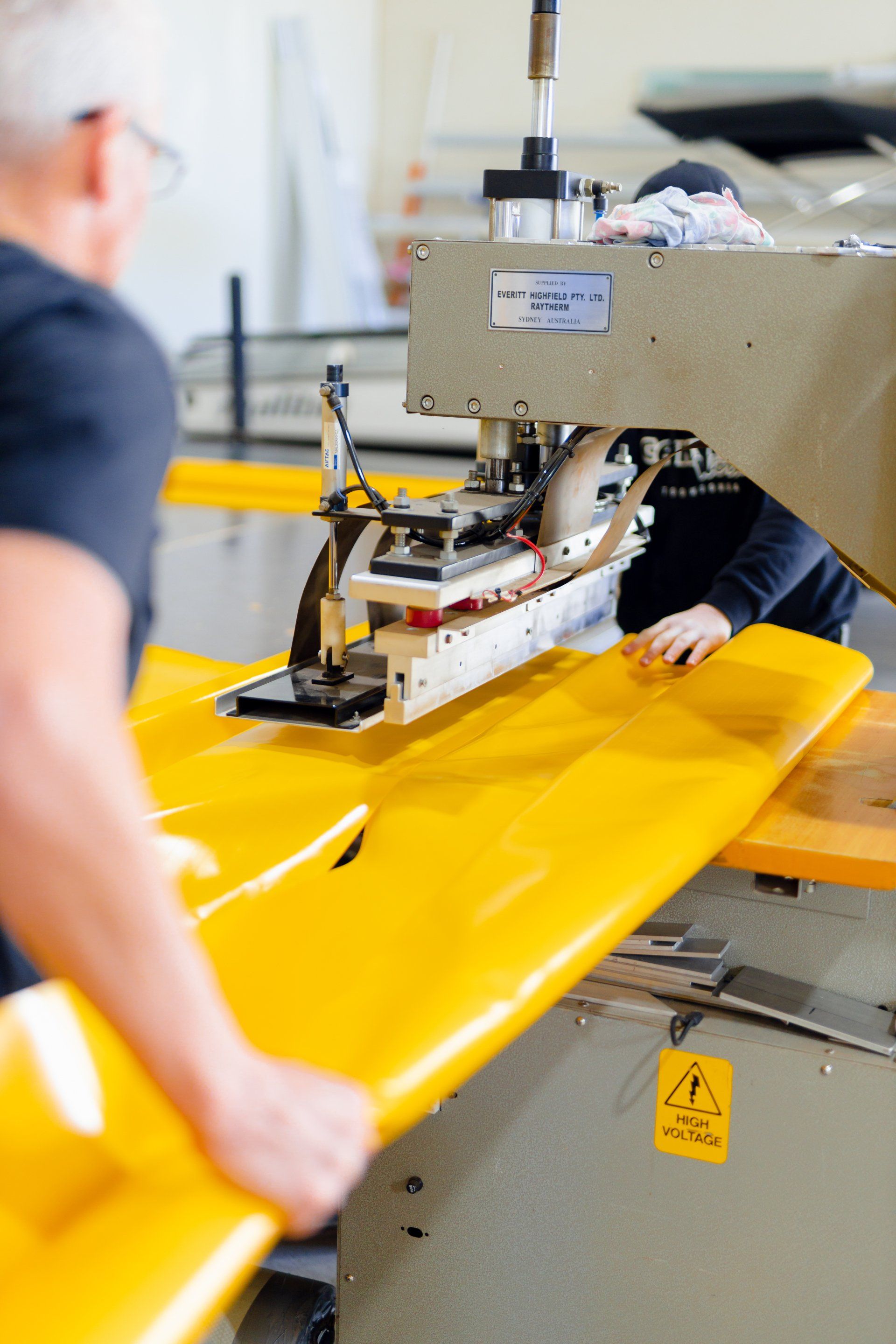 Worker operating a machine that seals bright yellow material in a factory